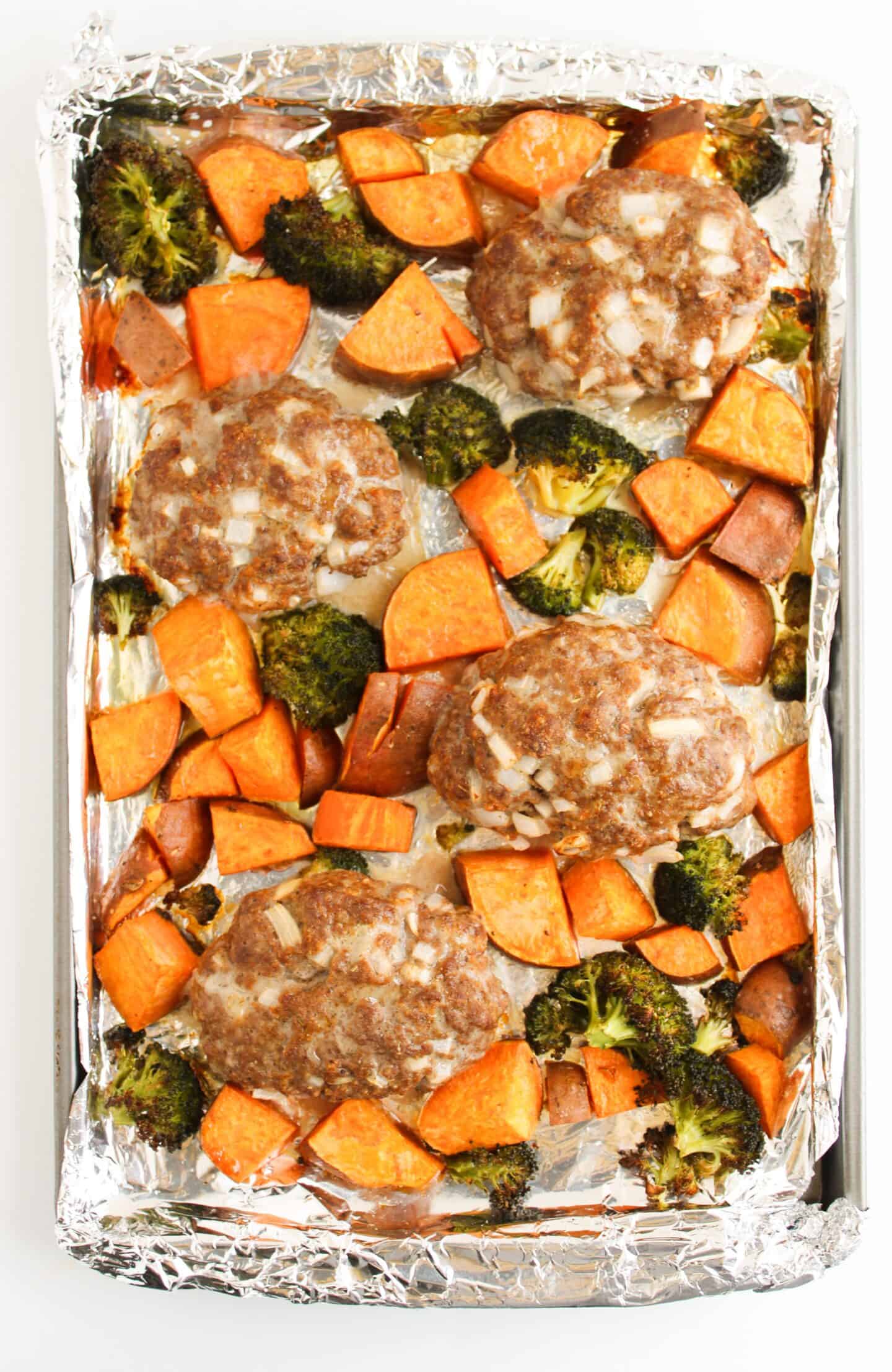 A foil-lined sheet pan showcases mini meatloaf alongside cubed sweet potatoes and vibrant veggies like broccoli florets.