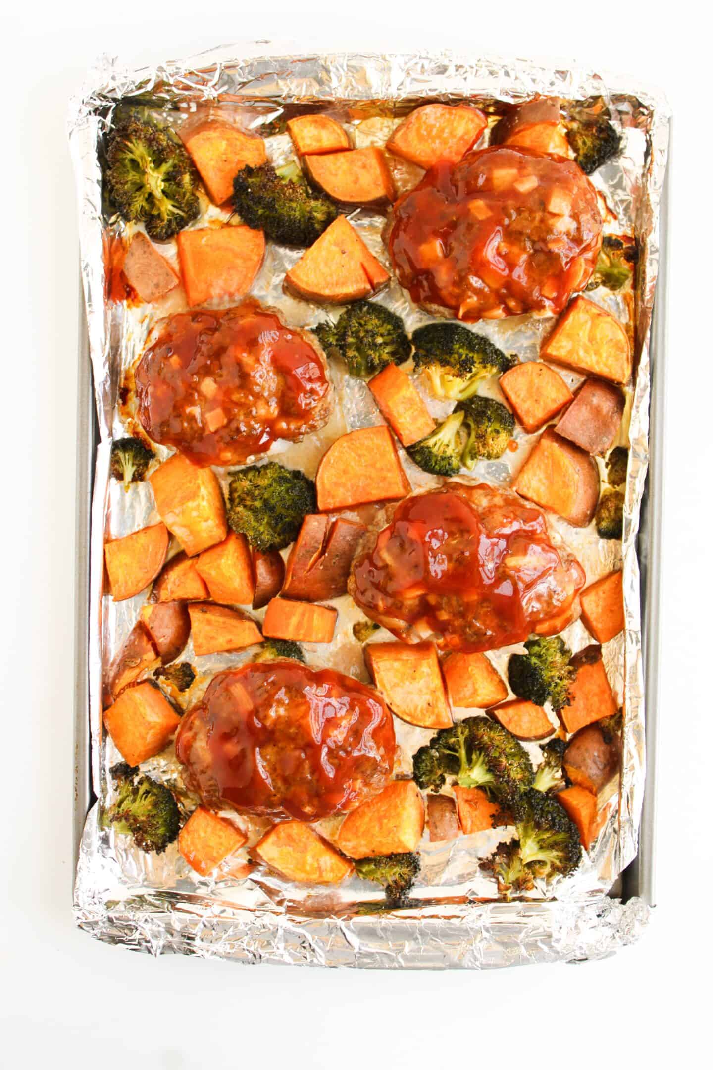 Savor this easy sheet pan meal featuring mini meatloaves with a tangy barbecue glaze, nestled alongside diced sweet potatoes and vibrant veggies like broccoli on foil.