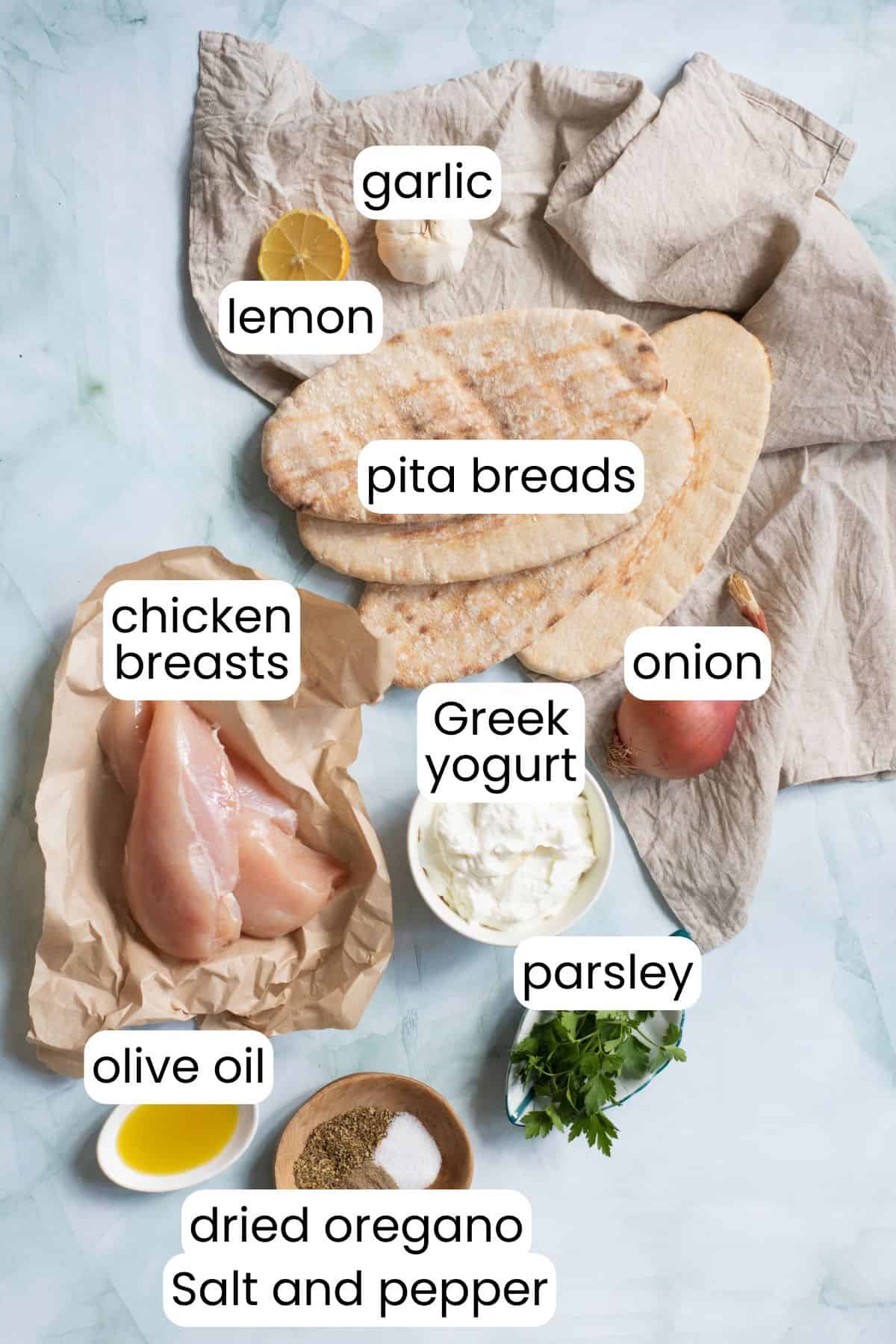 Ingredients for Chicken Pitas include raw chicken breasts, pita bread, and a refreshing yogurt sauce made with light yogurt, lemon, garlic, onion, fresh parsley, olive oil, dried oregano, salt, and pepper.