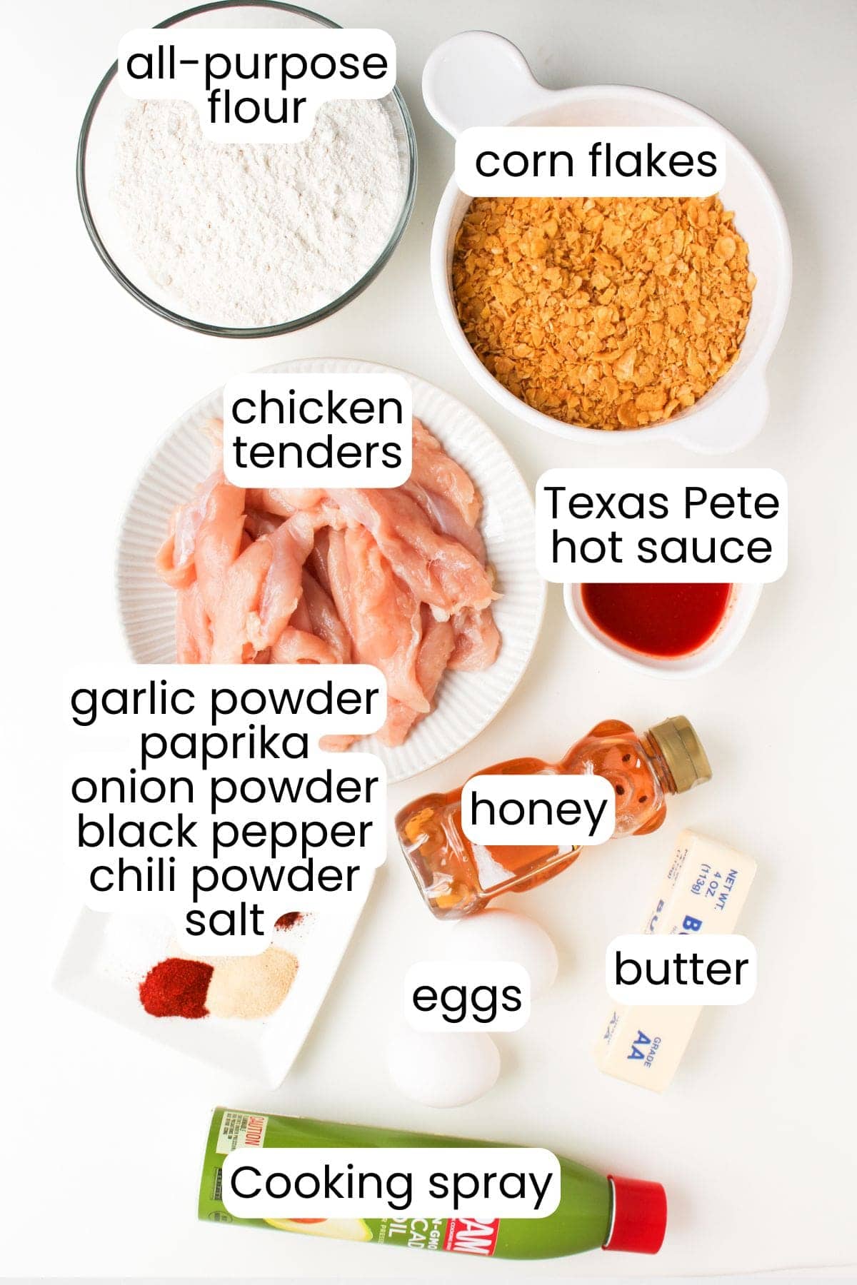 Chicken tenders, all-purpose flour, corn flakes, hot honey, butter, eggs, and spices are arranged on a white surface—perfect for making crispy Air Fryer Chicken Tenders with a spicy-sweet kick.