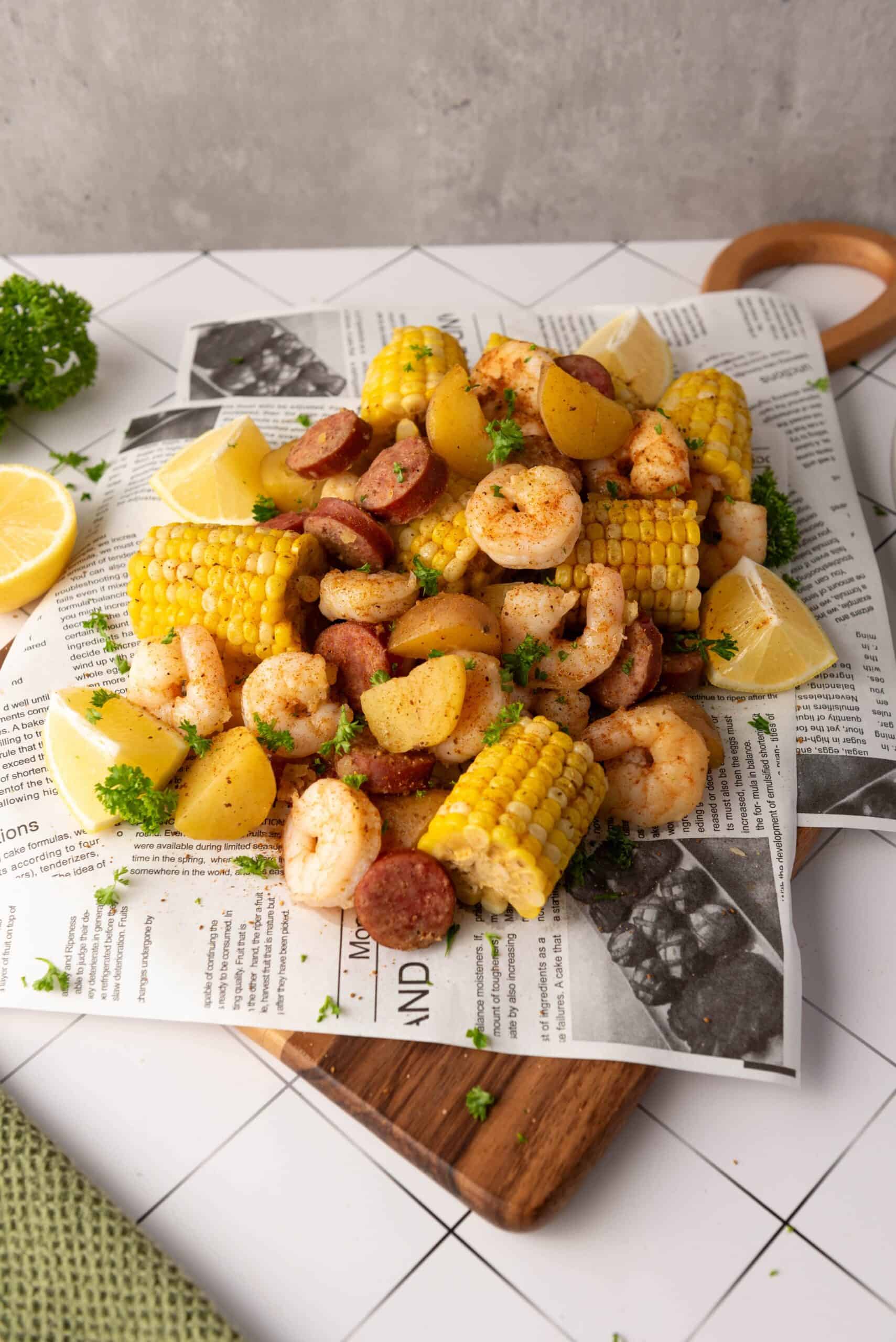 A serving of Shrimp Boil with sausage, corn on the cob, and potatoes garnished with parsley and lemon wedges, arranged on newspaper on a wooden tray—an easy recipe perfect for your Instant Pot.