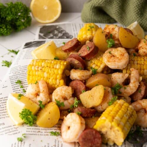 An Instant Pot Shrimp Boil with shrimp, sausage, corn, potatoes, and lemon wedges is served on newspaper and garnished with fresh parsley.