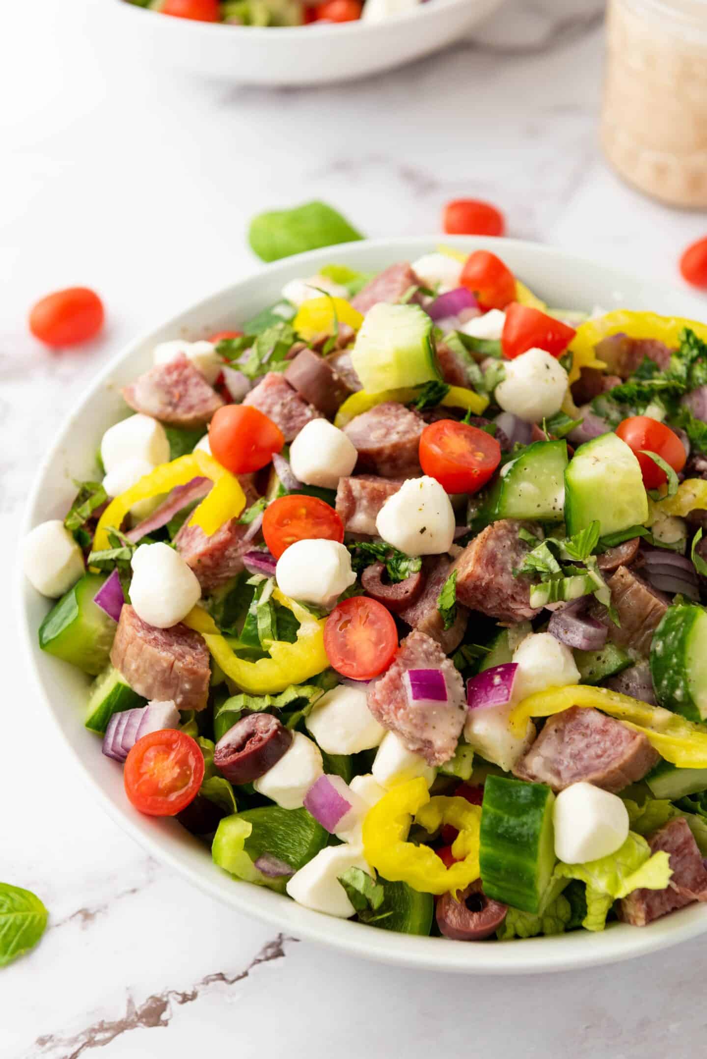 A bowl of Italian Chopped Salad with sliced sausage, cherry tomatoes, mozzarella balls, cucumber, red onion, olives, and pepper rings tossed in a zesty dressing.