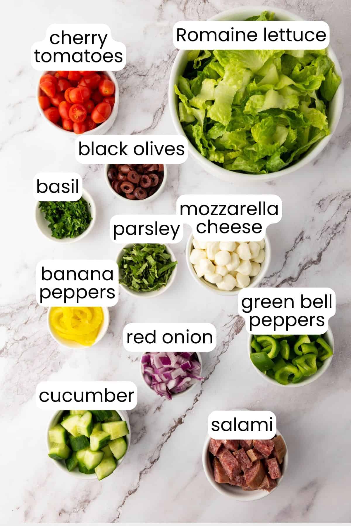 A flavorful Italian Chopped Salad featuring Romaine lettuce, cherry tomatoes, black olives, basil, parsley, mozzarella cheese, banana peppers, green bell peppers, red onion, cucumber, and salami—all tossed with a zesty dressing.