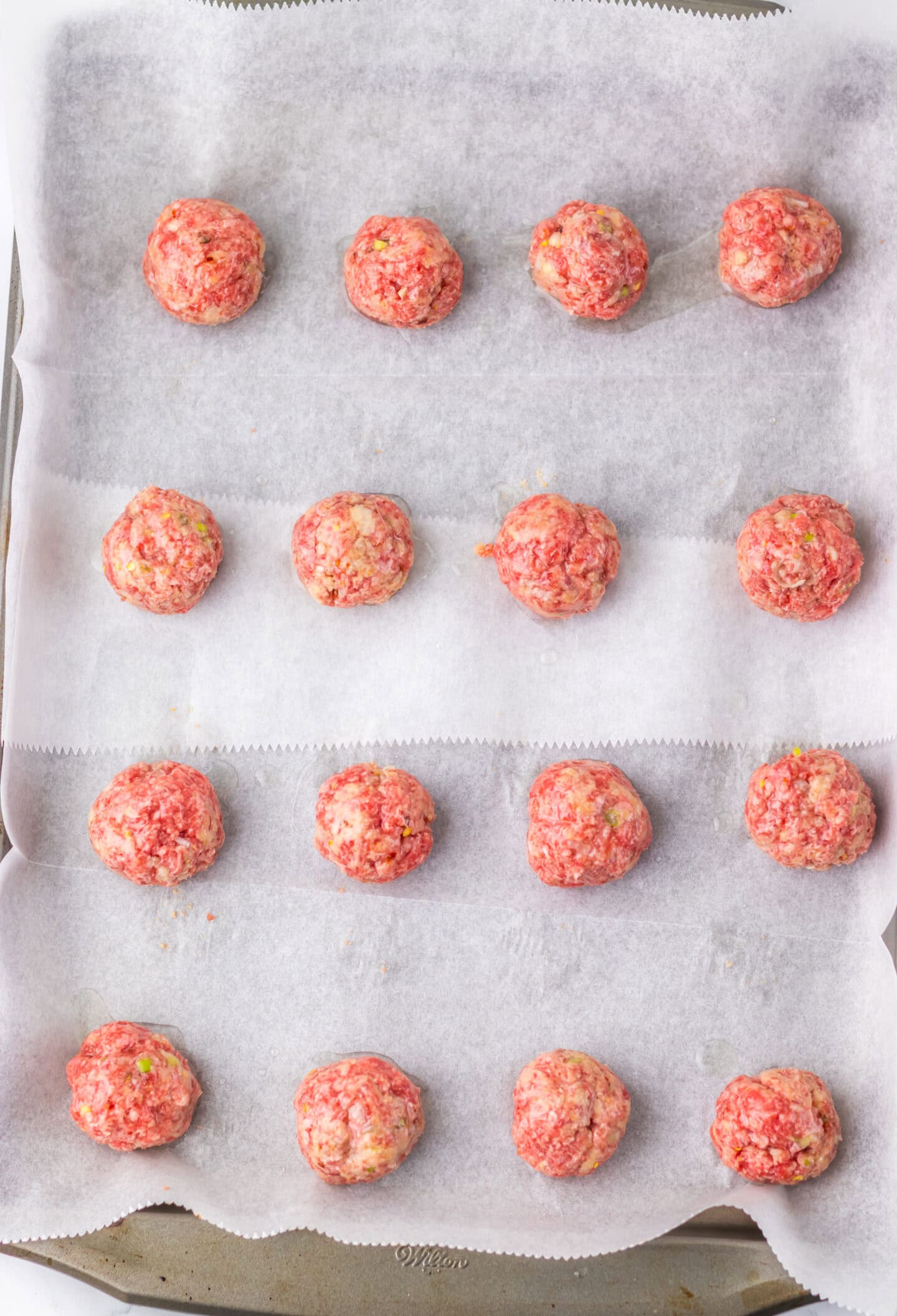 Raw Firecracker Meatballs arranged in rows on a baking sheet lined with parchment paper, ready to be cooked.