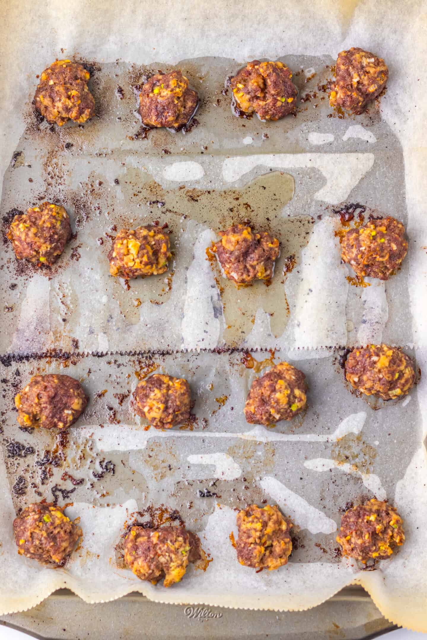 A baking tray lined with parchment paper holds rows of Firecracker Meatballs, each with browned spots and melted cheese.