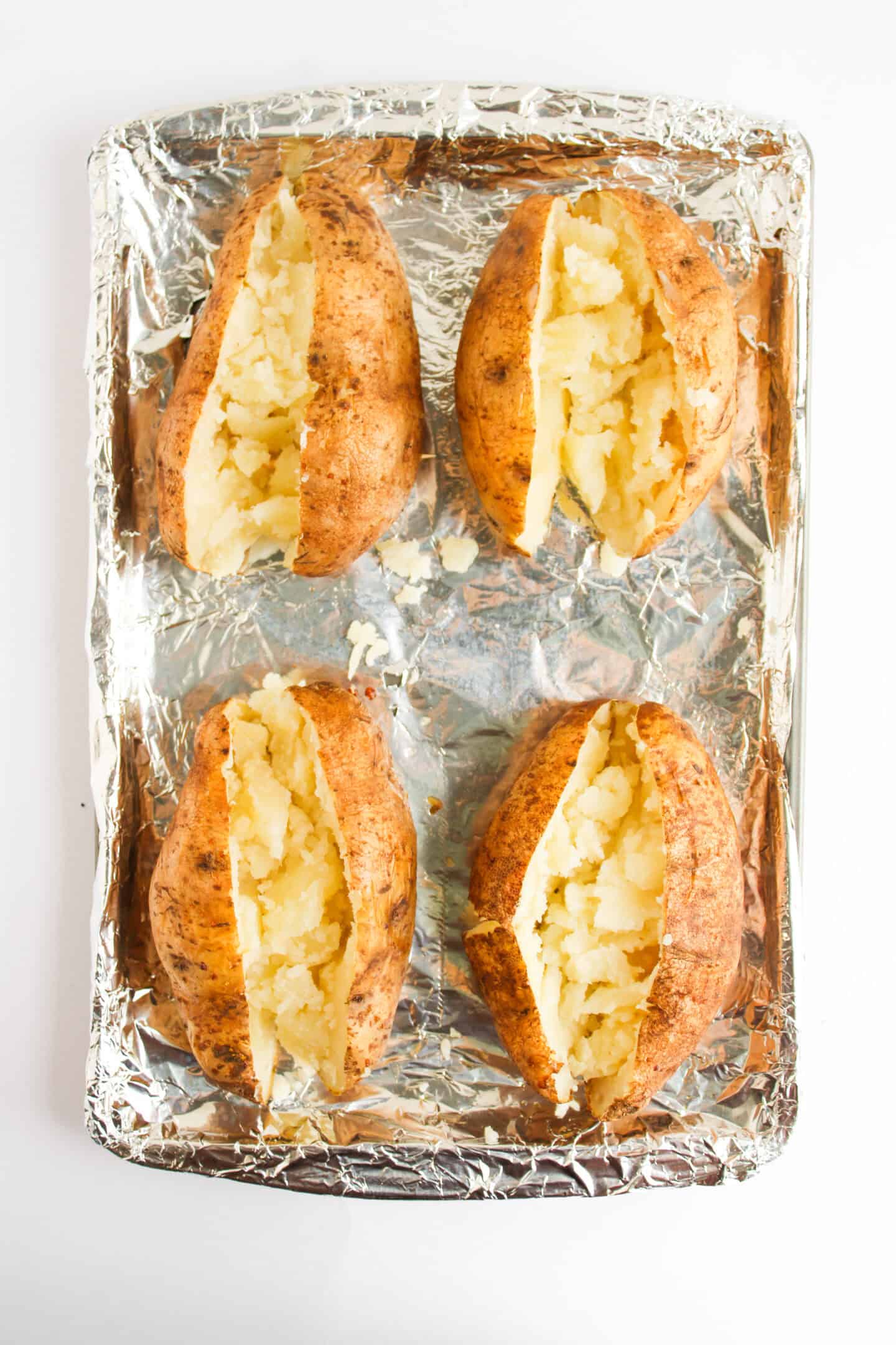 Four Buffalo Chicken Stuffed Baked Potatoes with split tops are arranged on a foil-lined baking sheet.