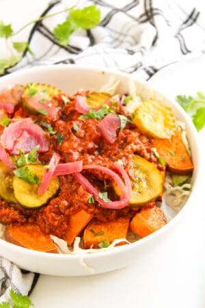 A bowl inspired by Sloppy Joe Bowls, featuring sweet potato slices, shredded cabbage, pickled onions, cooked ground meat in tomato sauce, and zucchini slices, all garnished with cilantro.