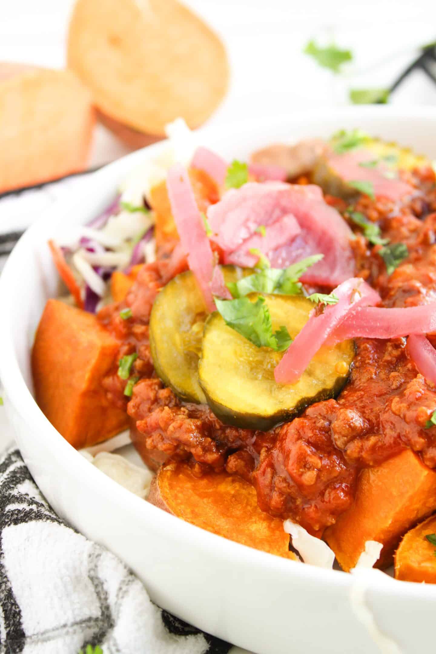 A white bowl filled with sweet potato chunks, zucchini slices, shredded cabbage, chili, and pickled red onions, garnished with chopped herbs—a fresh take on Sloppy Joe Bowls for a wholesome twist.