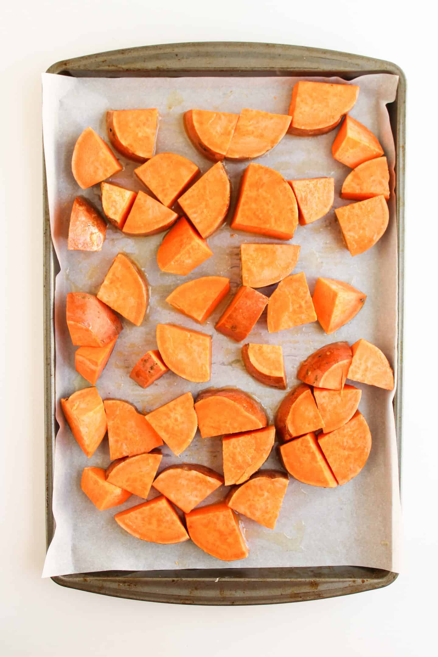 A baking tray lined with parchment paper holds evenly spaced, raw sweet potato chunks ready for roasting—perfect for assembling easy dinner Sloppy Joe Bowls.