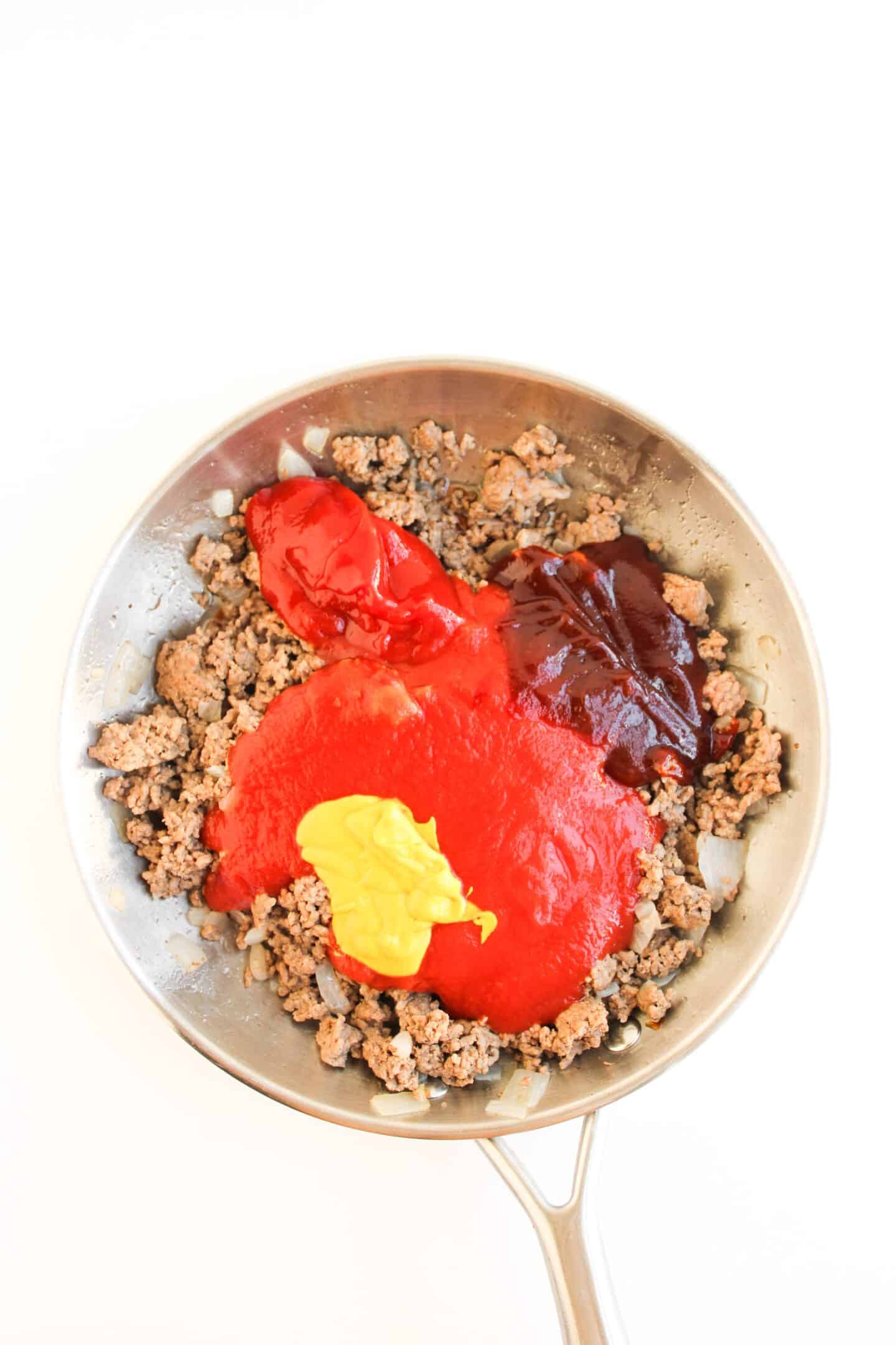 A skillet with cooked ground beef and onions topped with ketchup, mustard, tomato sauce, and barbecue sauce—a delicious twist on classic Sloppy Joe Bowls, viewed from above.