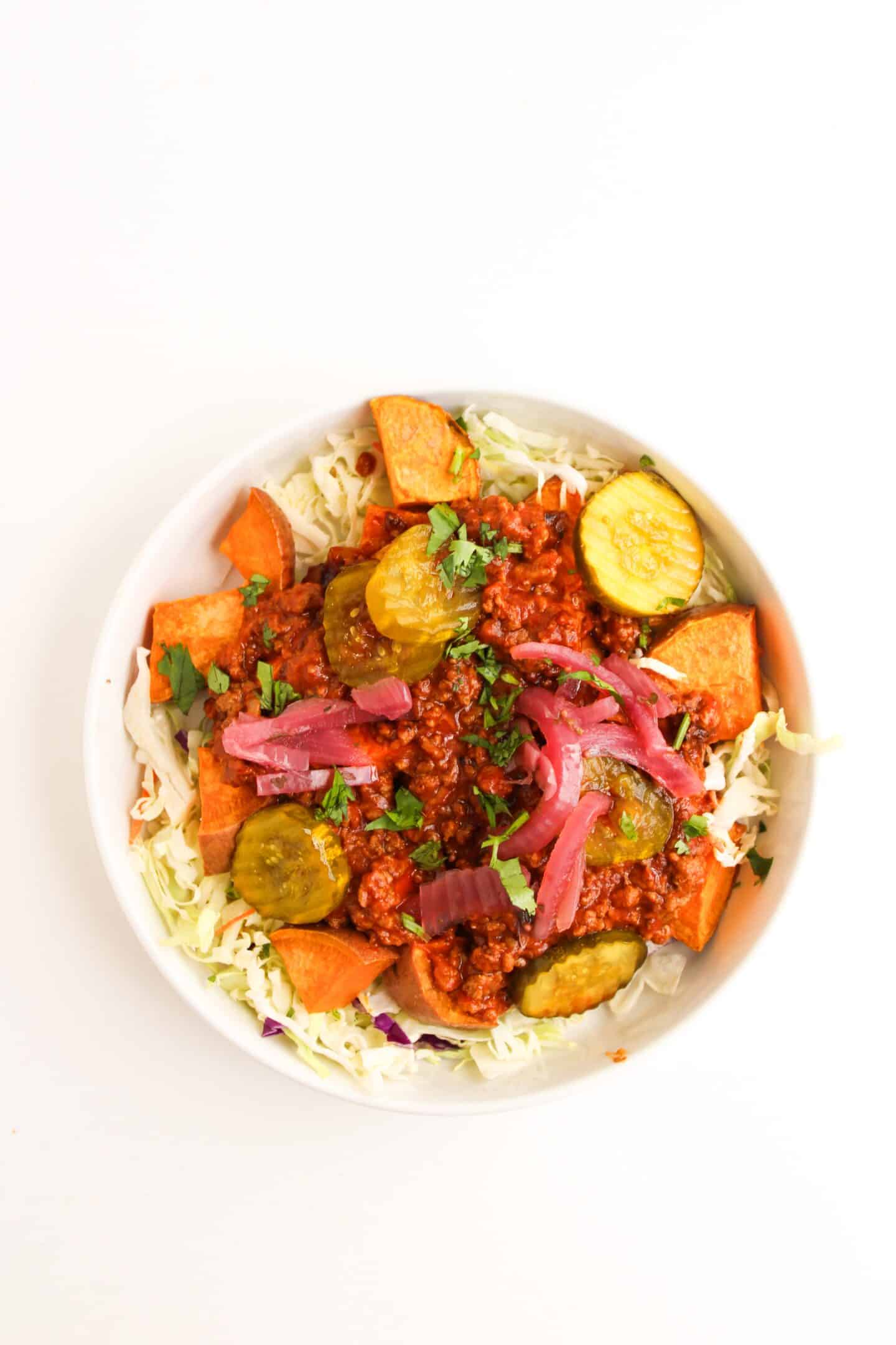 A flavorful Bowl Recipe featuring shredded cabbage, roasted sweet potatoes, saucy Sloppy Joe ground meat, pickles, and red onions, all garnished with fresh herbs.