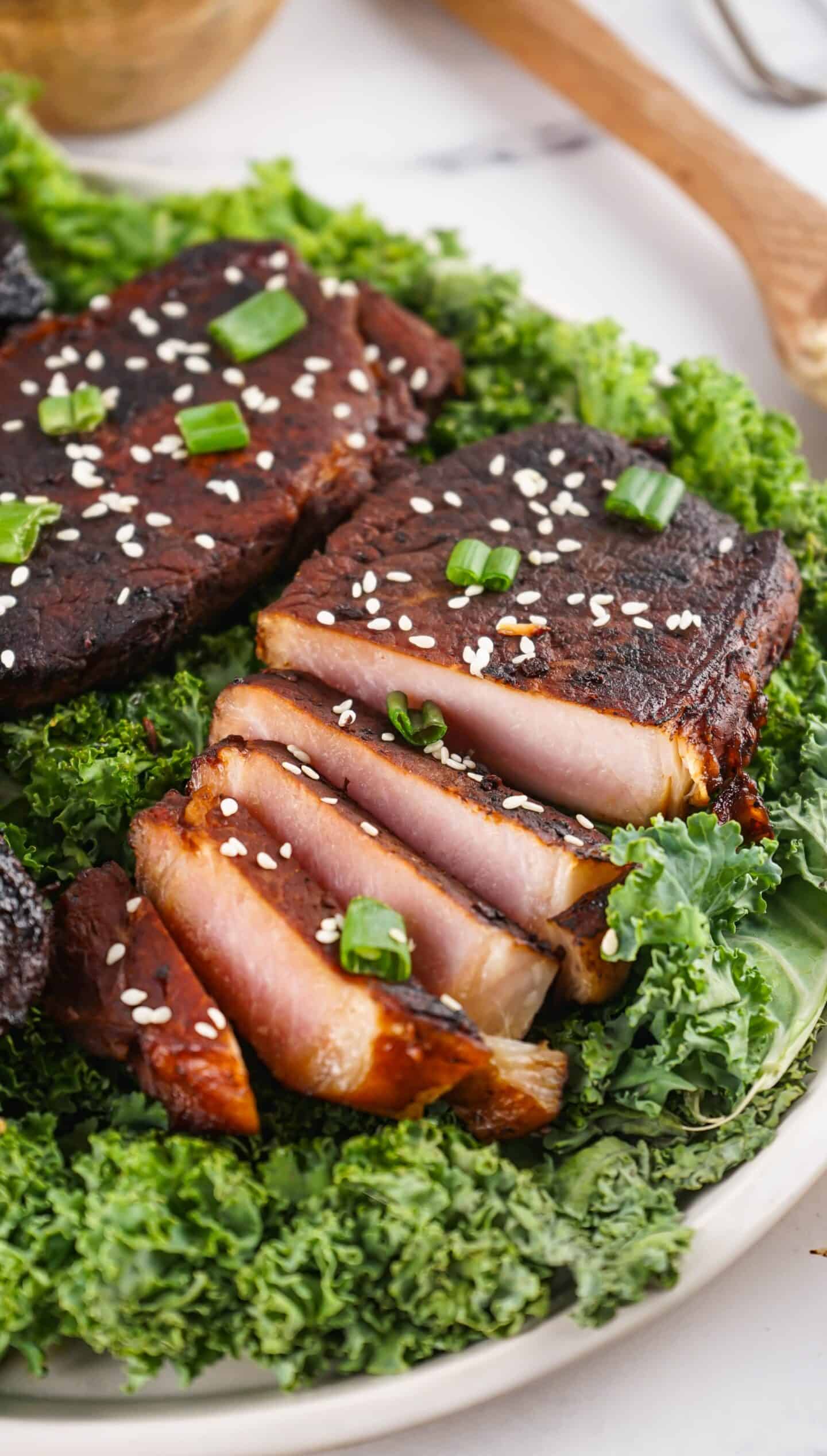 Slices of seared tuna steak with a dark crust, topped with sesame seeds and chopped green onions, served on a bed of leafy greens—perfect for those who enjoy Asian Style Pork Chops but crave seafood.