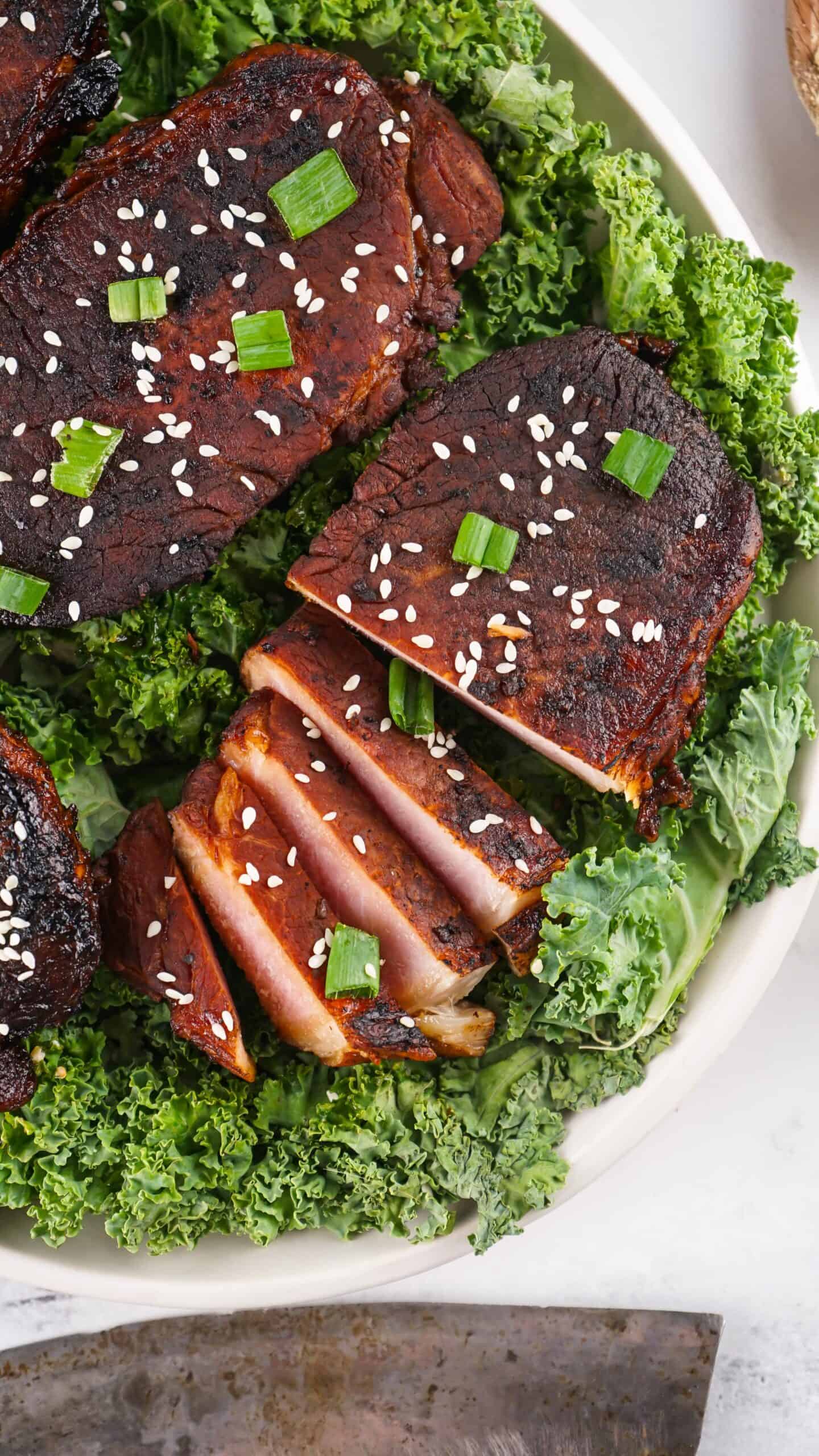 Grilled, sliced tuna steaks topped with sesame seeds and chopped green onions, served on a bed of fresh kale—perfect for fans of Asian Style Pork Chops seeking a lighter seafood twist.