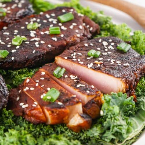 Several pieces of seared tuna steak, garnished with sesame seeds and chopped green onions, are served on a bed of fresh kale for a dish inspired by the bold flavors found in Asian Style Pork Chops.
