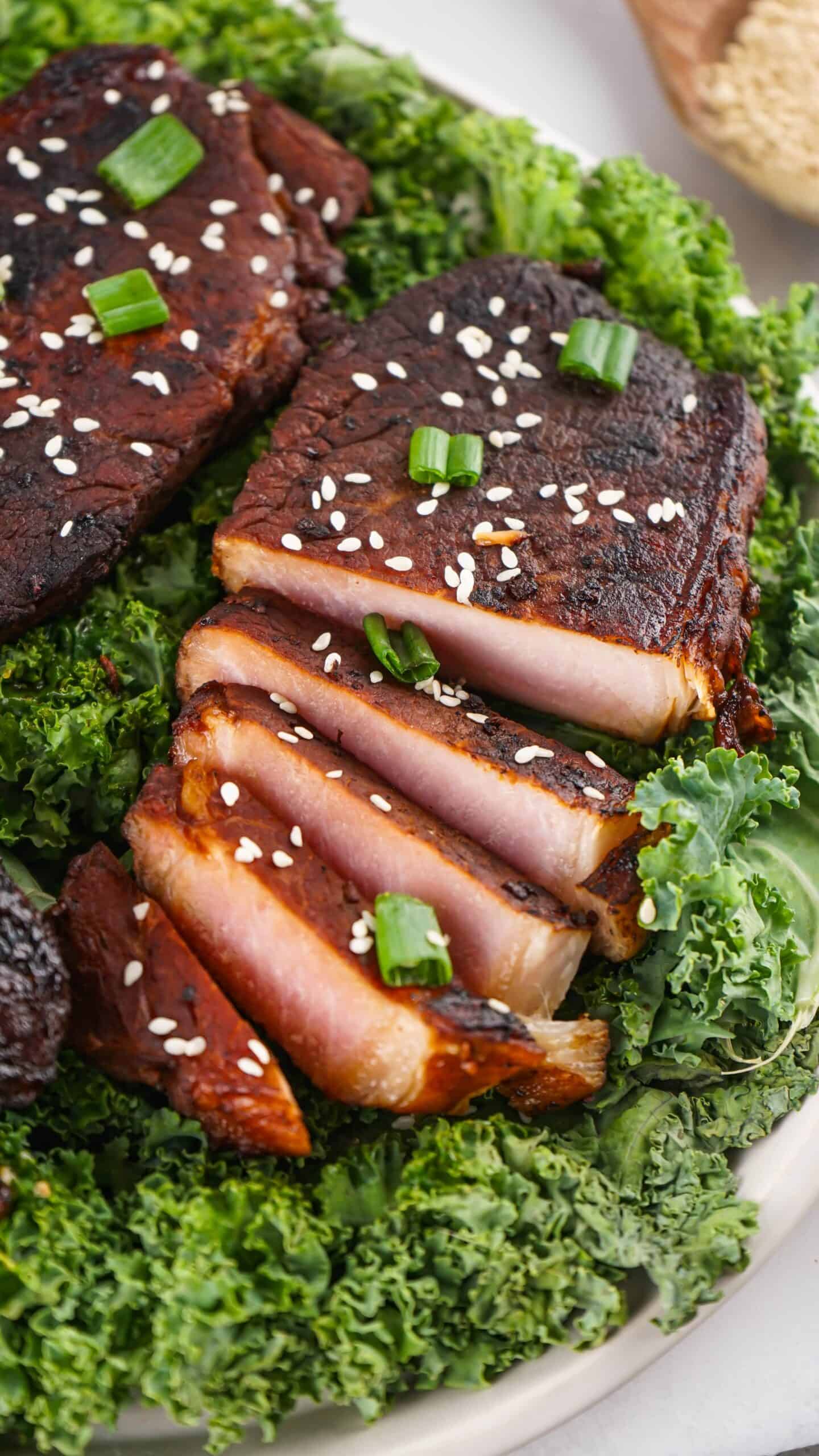 Sliced seared tuna topped with sesame seeds and chopped green onions, served on a bed of fresh kale—an ideal complement to our Asian Style Pork Chops for a flavorful meal.