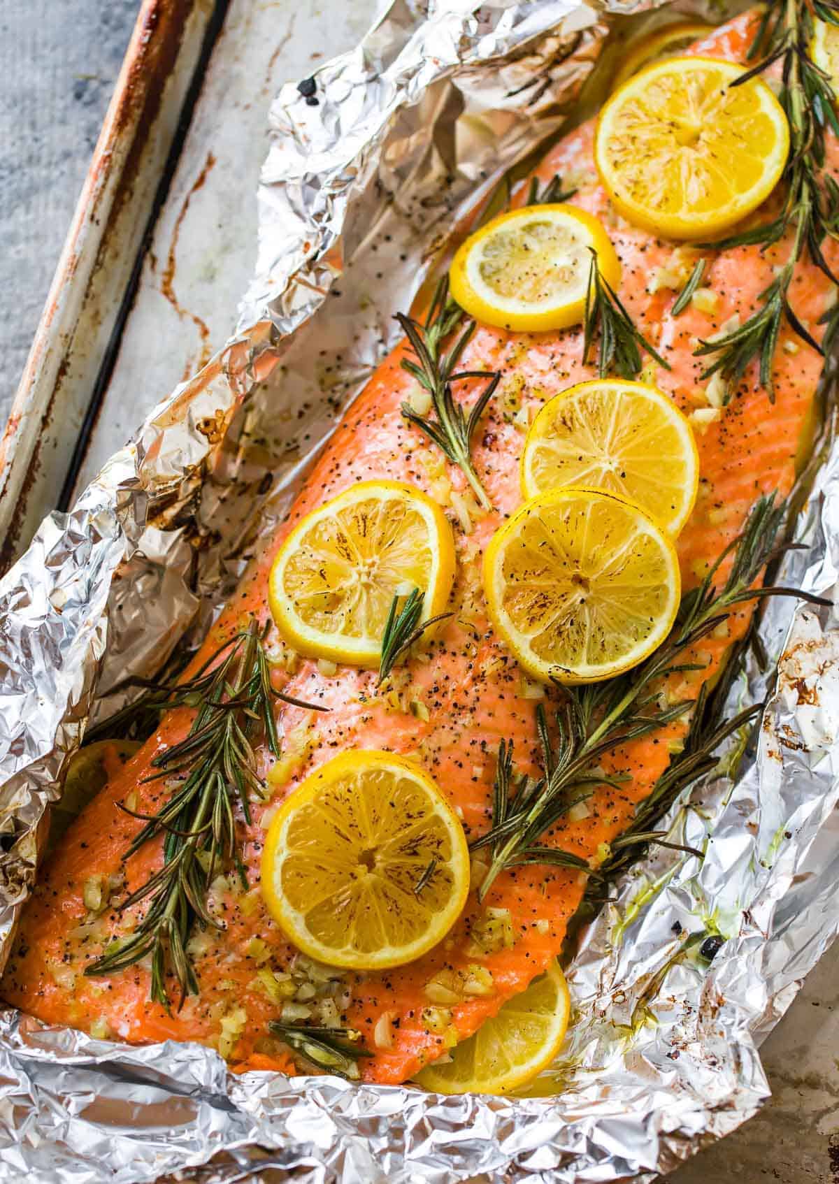Salmon fillet baked in foil with slices of lemon, sprigs of rosemary, minced garlic, and black pepper on a metal tray—one of the coziest Fall Salmon Recipes to savor this season.