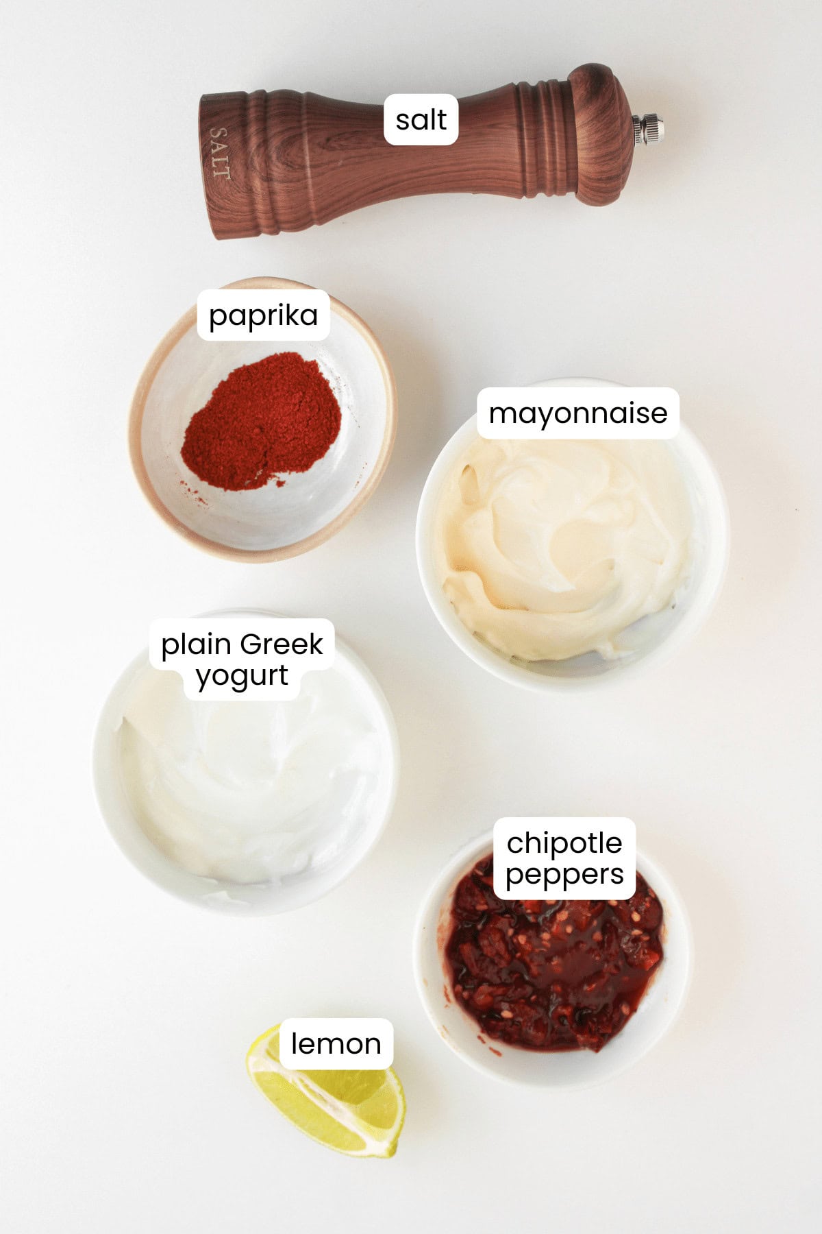 Five labeled ingredients for a chipotle sauce: salt in a grinder, paprika, mayonnaise, plain Greek yogurt, chopped chipotle peppers, and a lemon wedge—perfect for adding bold flavor to Shrimp Fajita Bowls or any fajita bowls.