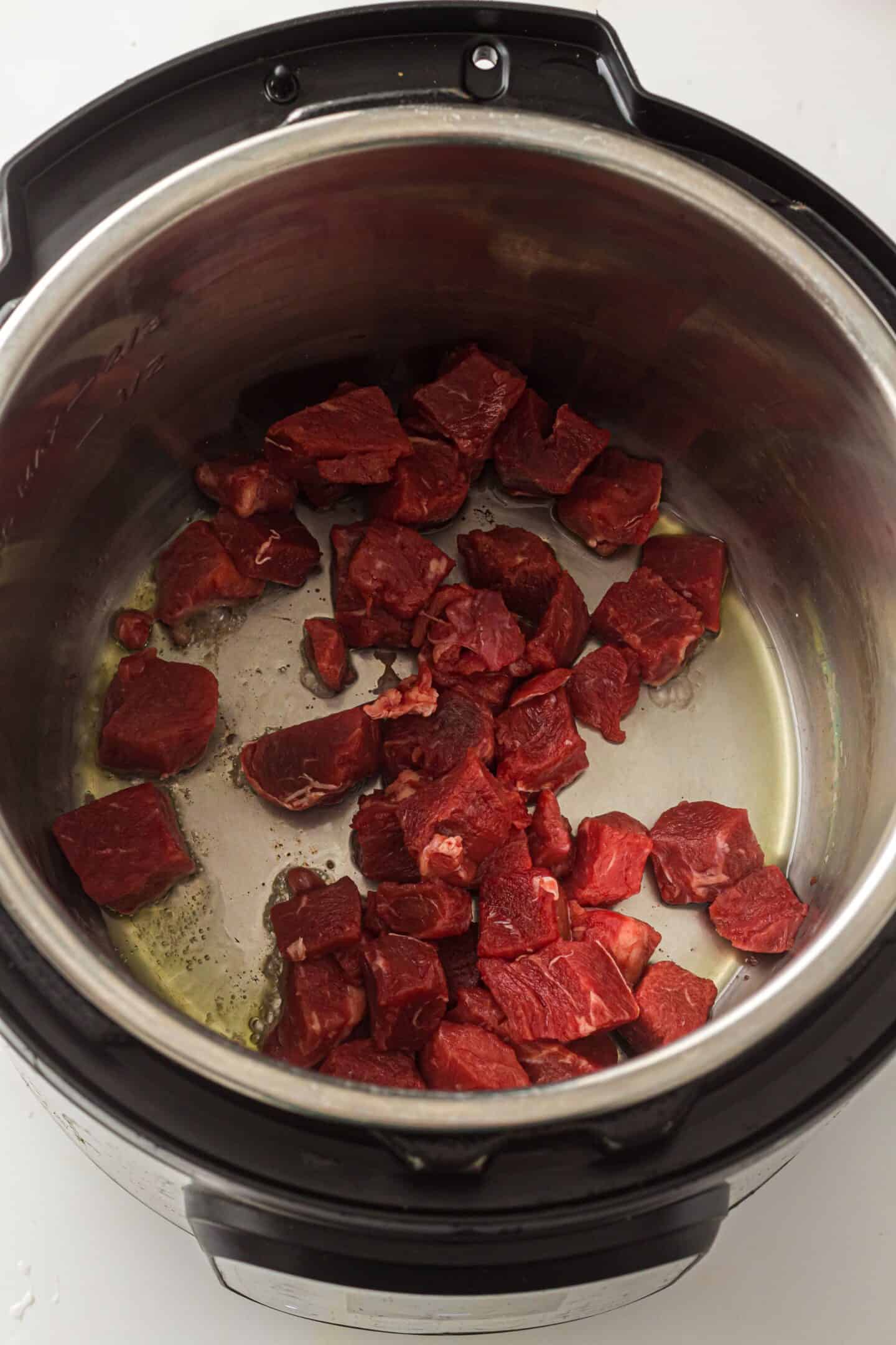 Cubed raw beef placed in the inner pot of an Instant Pot, ready for cooking a hearty beef stew.