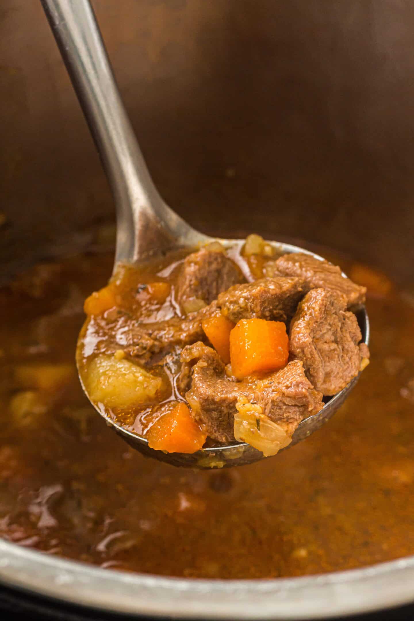A metal ladle holds a serving of hearty Beef Stew with chunks of beef, carrots, and potatoes over an Instant Pot filled with simmering stew.