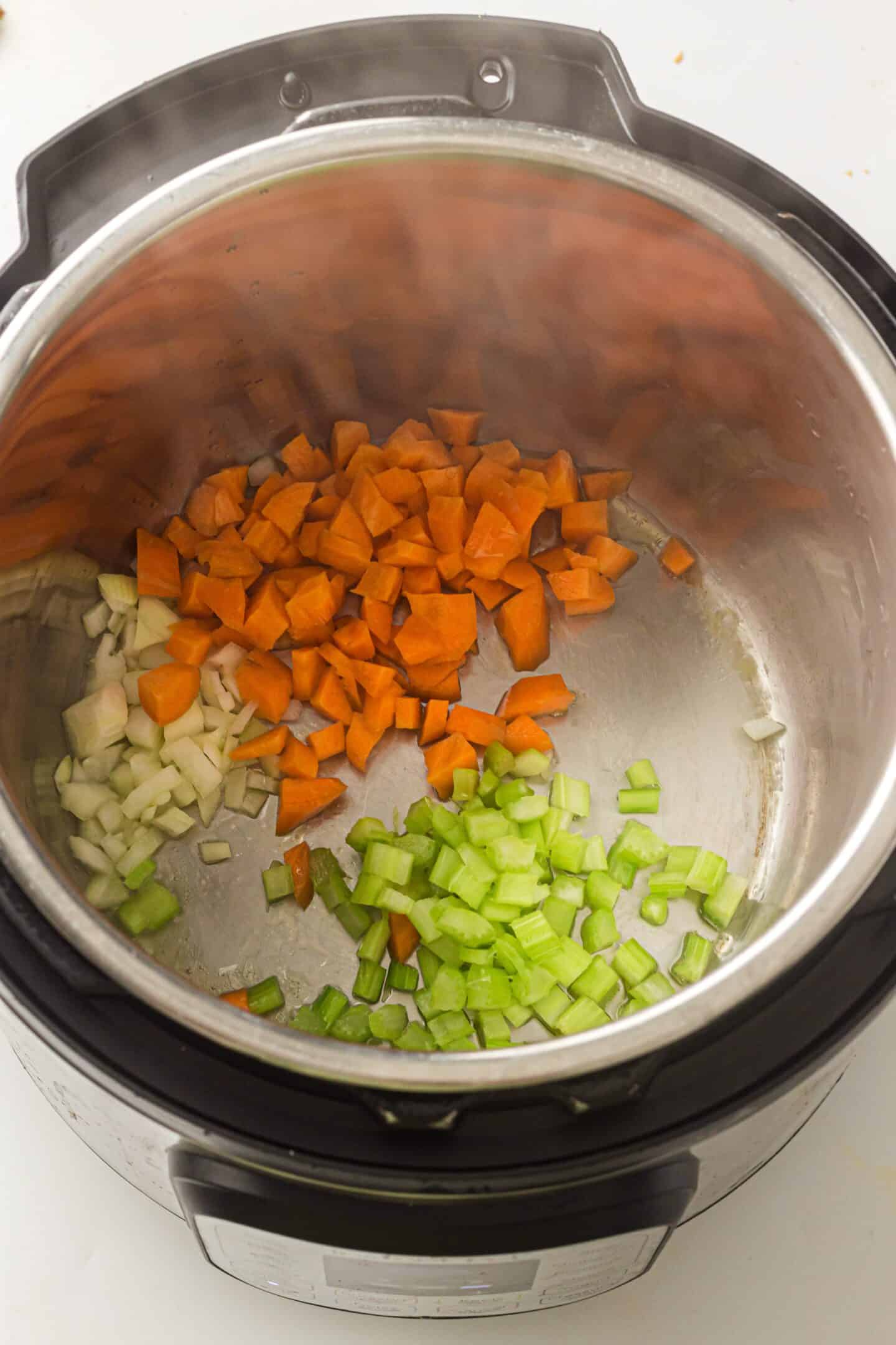 Chopped carrots, celery, and onions are sautéing in an Instant Pot, creating the perfect flavorful base for Instant Pot Chicken Noodle Soup.