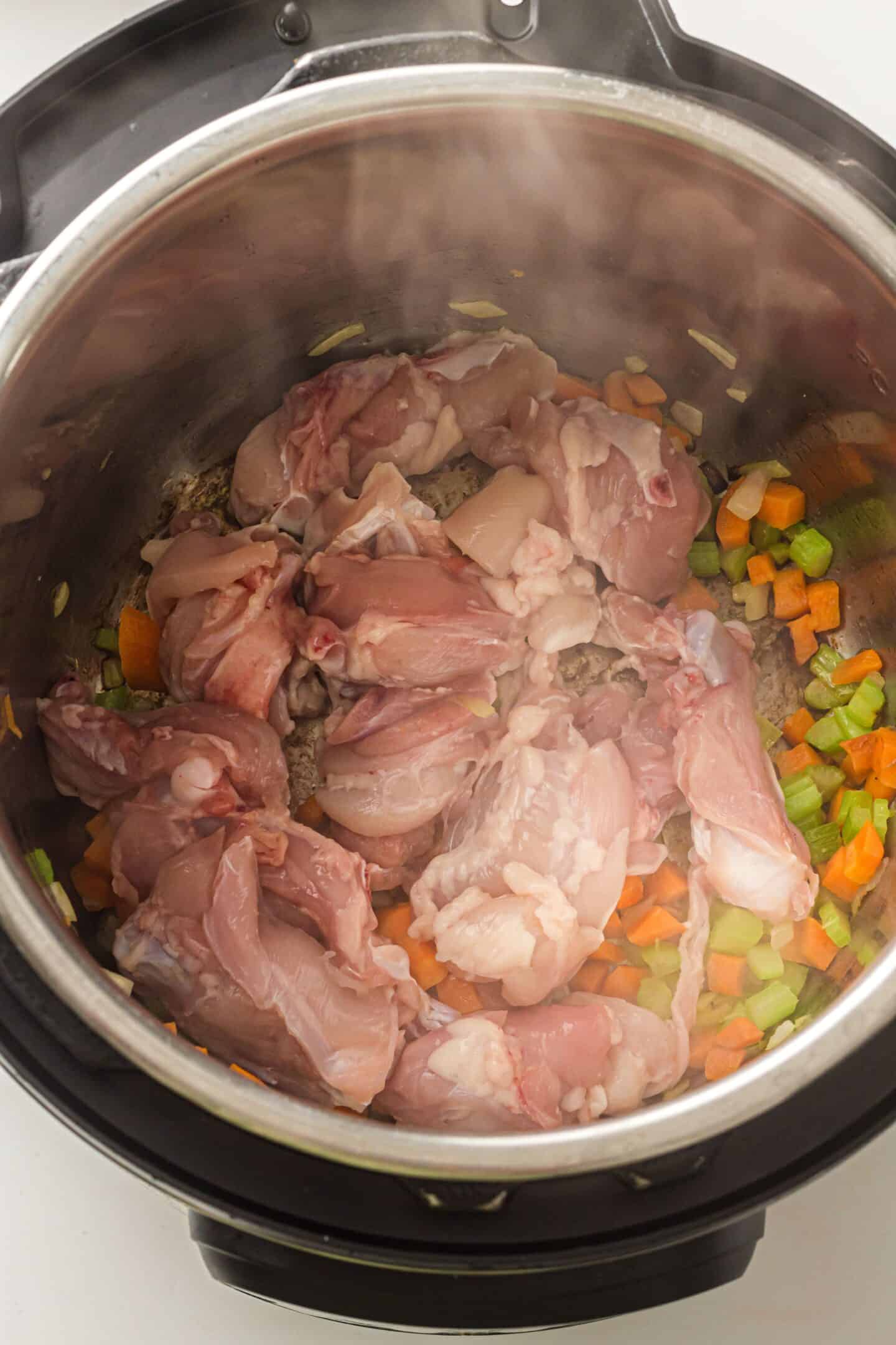Raw chicken pieces placed on top of chopped carrots, celery, and onions inside an Instant Pot, ready to become a comforting Instant Pot Chicken Noodle Soup.