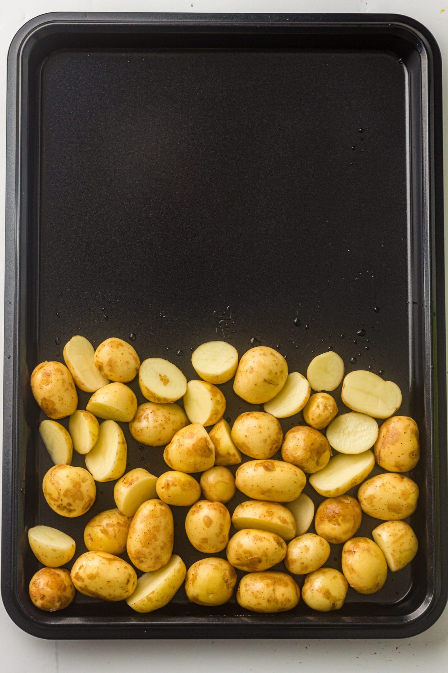 A sheet pan with halved and whole baby potatoes arranged on one side, ready for roasting alongside BBQ chicken thighs.