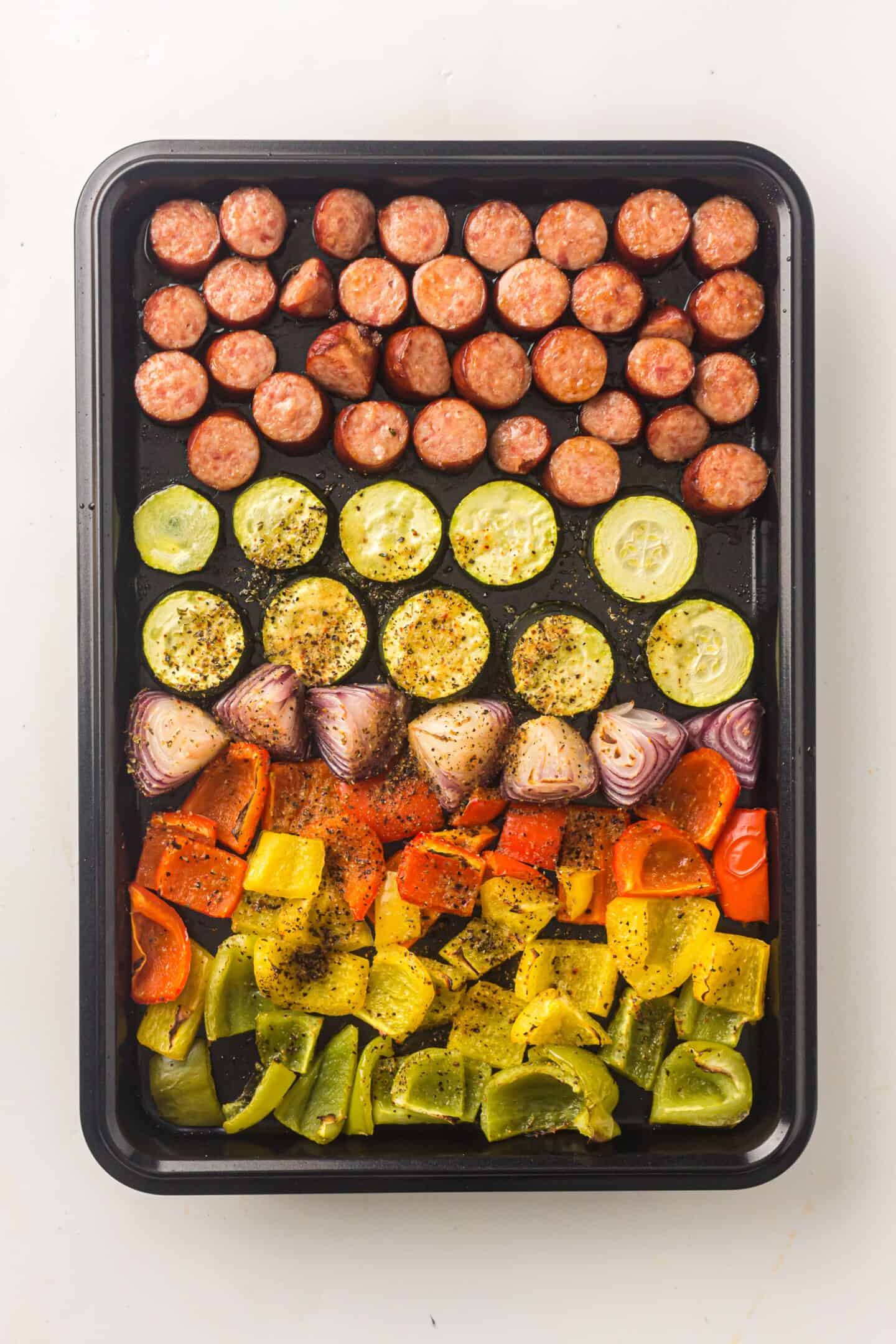 A sheet pan lined with rows of chicken sausage, zucchini, red onion, and colorful bell peppers—these roasted vegetables are perfectly seasoned and ready to cook.