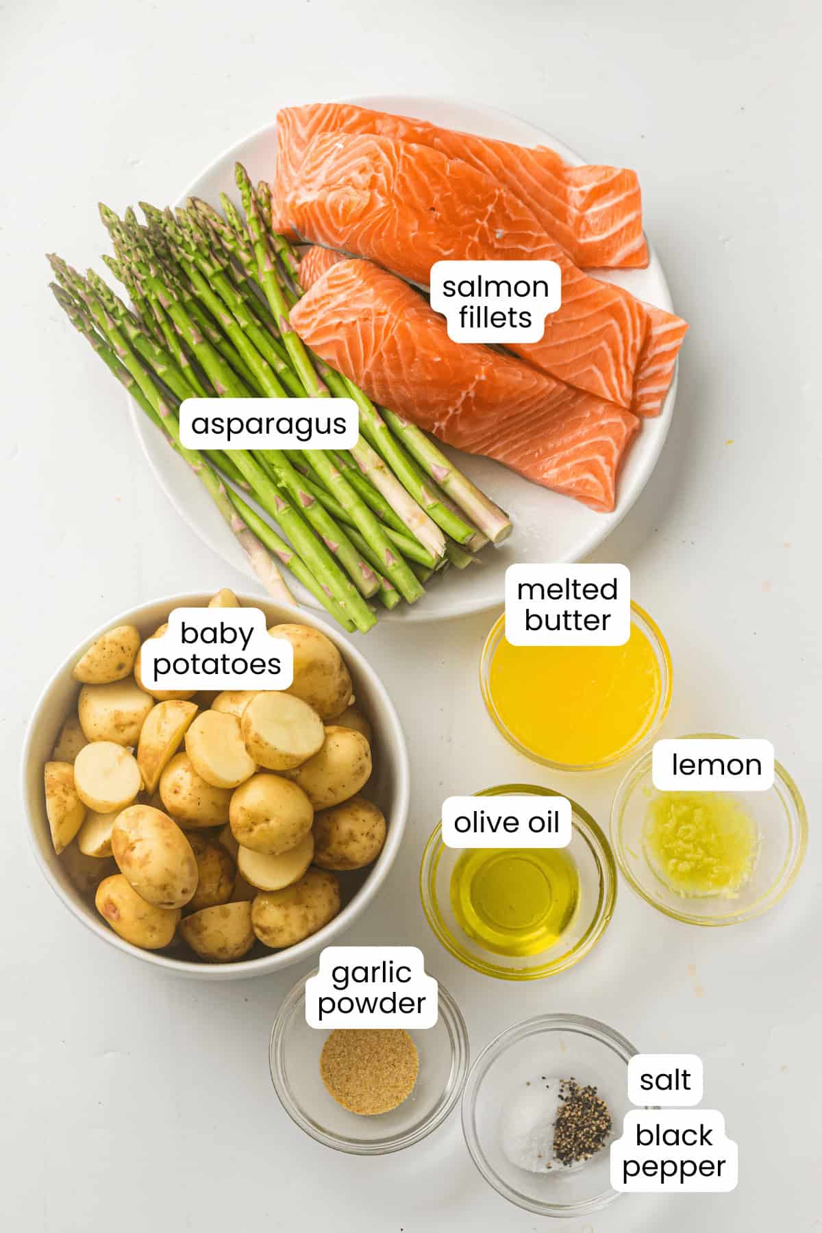 Sheet Pan Salmon with asparagus and roasted potatoes, drizzled with melted butter, olive oil, lemon juice, garlic powder, salt, and black pepper—all beautifully arranged on a white surface.
