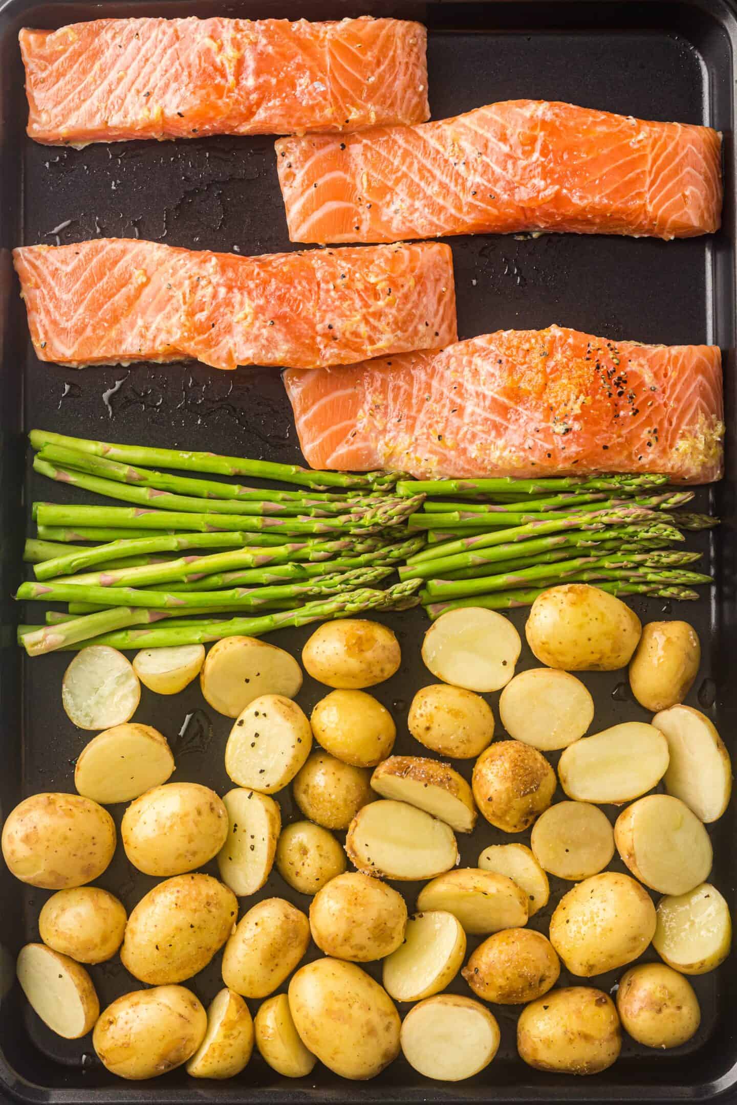 Sheet Pan Salmon with asparagus spears and roasted potatoes, all seasoned with salt and pepper, arranged on a baking sheet and ready to be cooked.