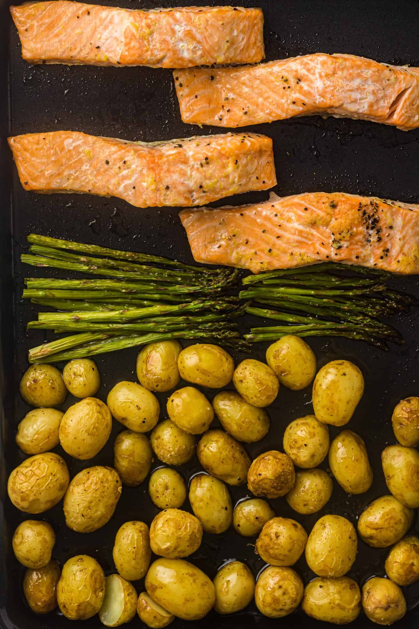 Sheet Pan Salmon fillets, asparagus spears, and roasted potatoes are arranged on a baking tray, ready for roasting.