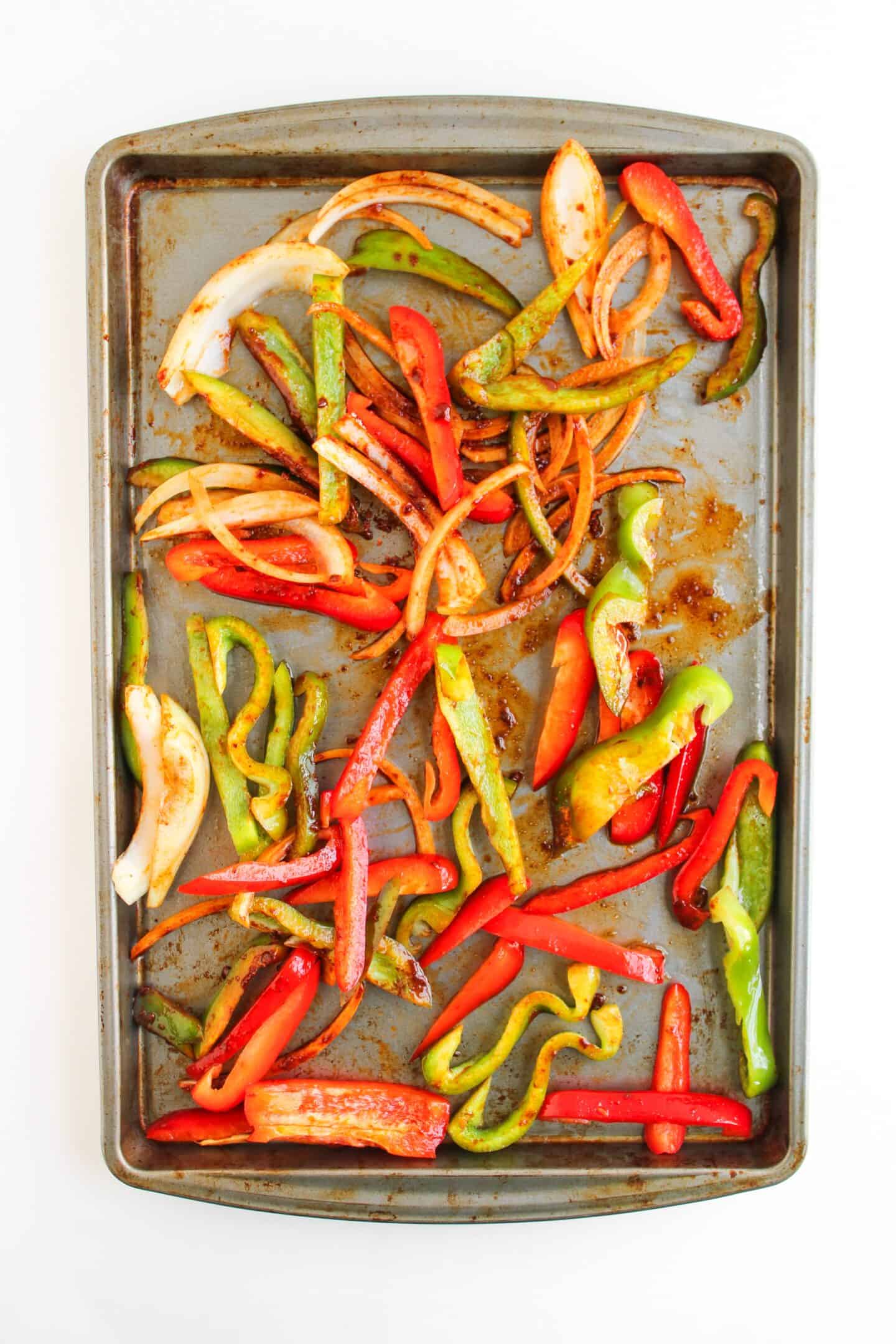 A baking sheet with roasted sliced red and green bell peppers and onions, lightly seasoned—perfect for adding vibrant flavor to Fajita Bowls or drizzling with chipotle sauce for an extra kick. Set on a clean white background.