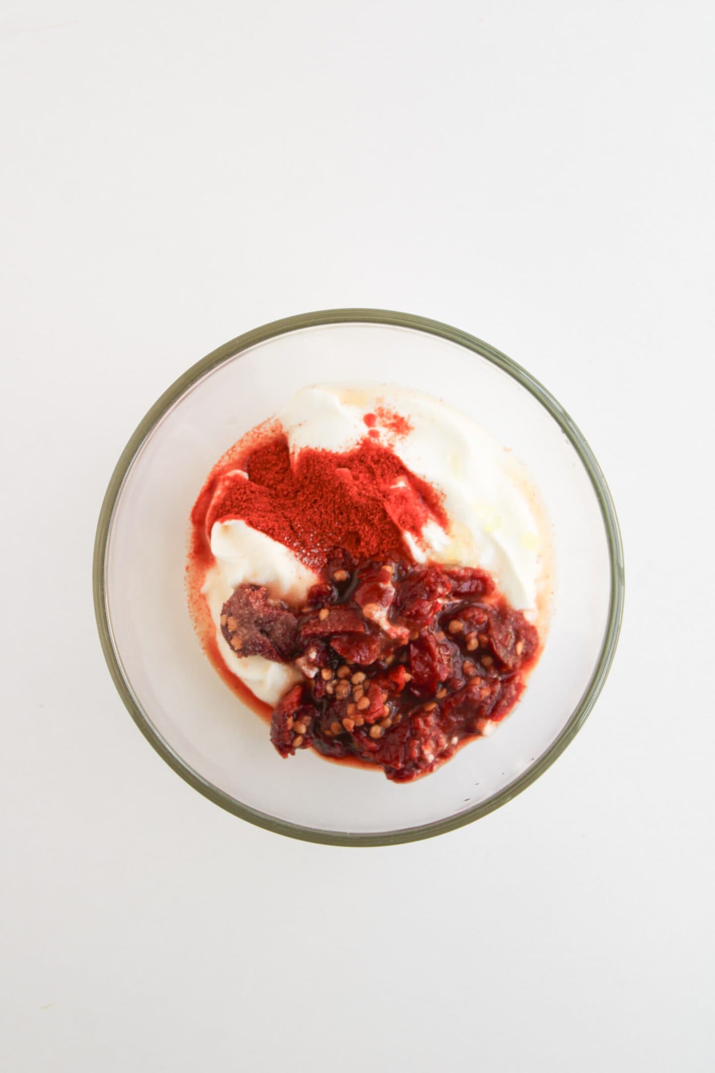 A glass bowl with yogurt, red berry compote, and red powder on top, placed on a white surface—perfect as a sweet contrast to spicy Shrimp Fajita Bowls or alongside your favorite Fajita Bowls with chipotle sauce.
