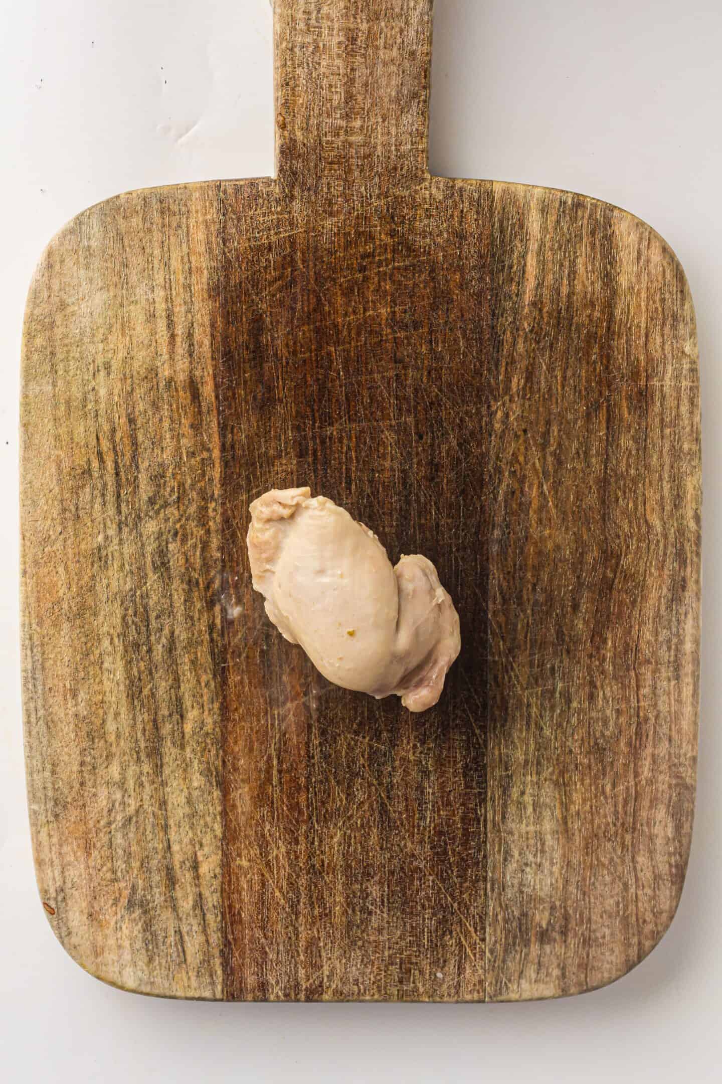 A single piece of cooked chicken breast, perfect for Slow Cooker White Chicken Chili, rests on a worn wooden cutting board.