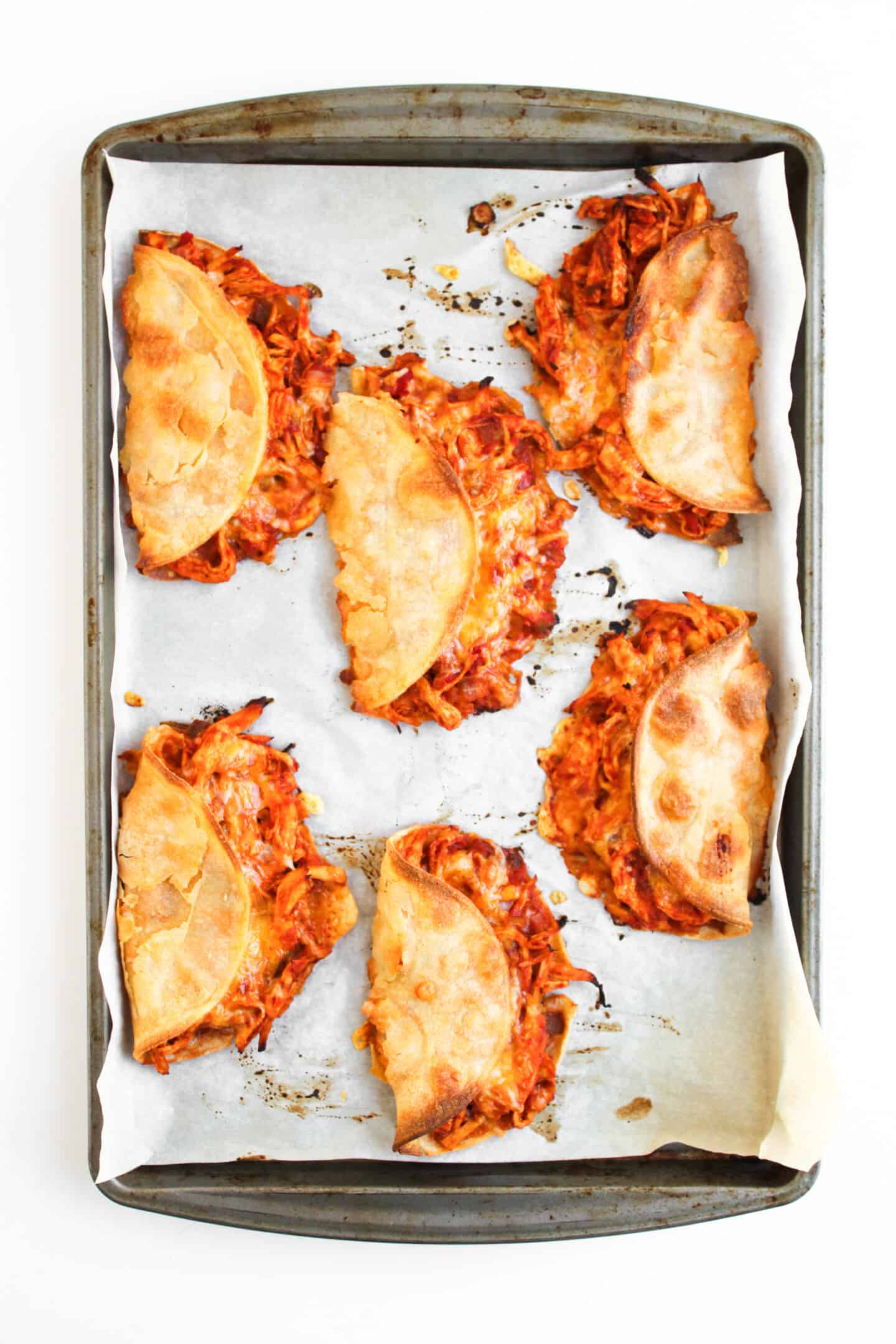 Six Crispy Baked Chicken Tacos filled with shredded meat and cheese, served on a parchment-lined baking sheet.