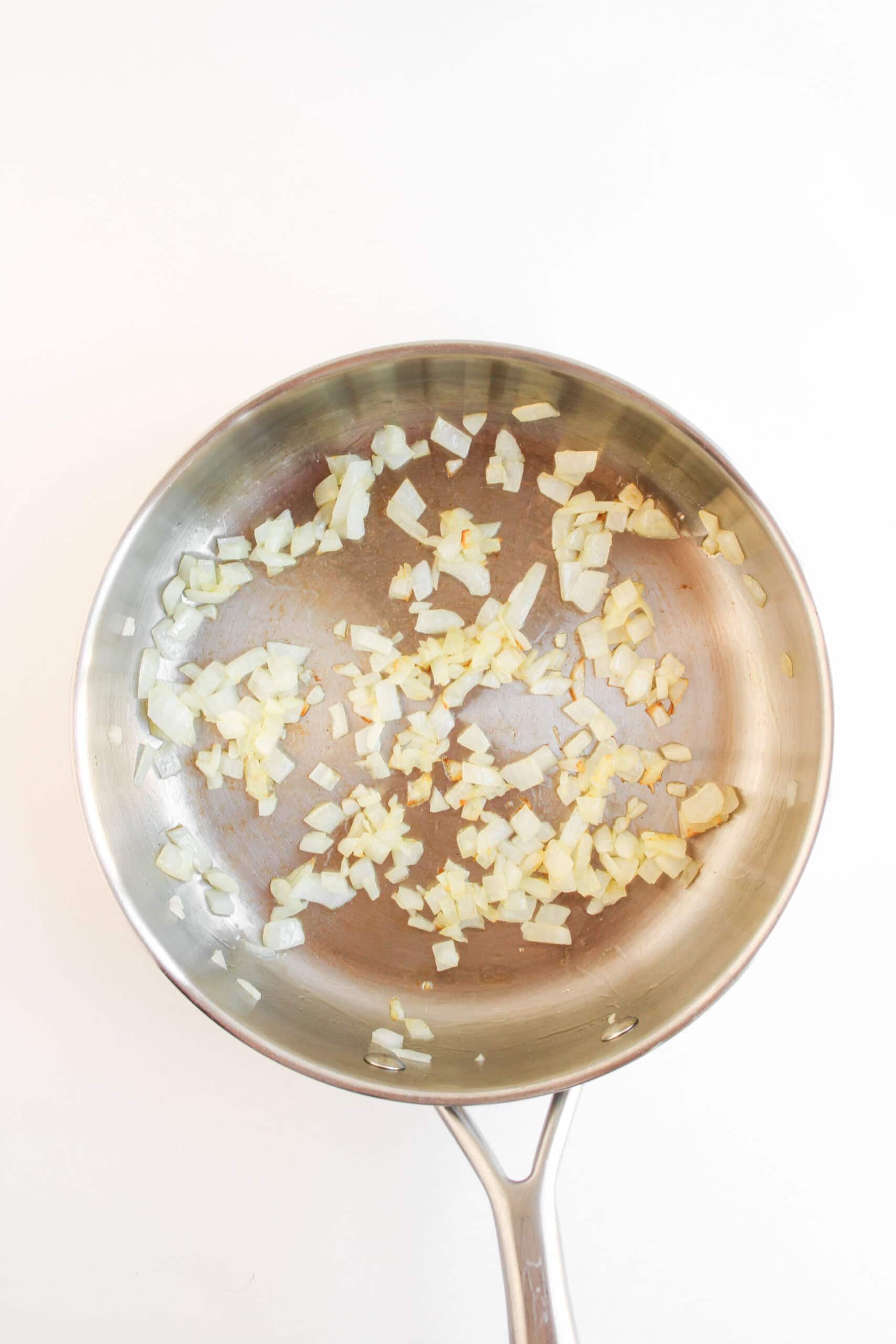 A stainless steel pan with chopped onions being sautéed, shown from above on a white background—perfect for prepping fillings like those in Crispy Baked Chicken Tacos.