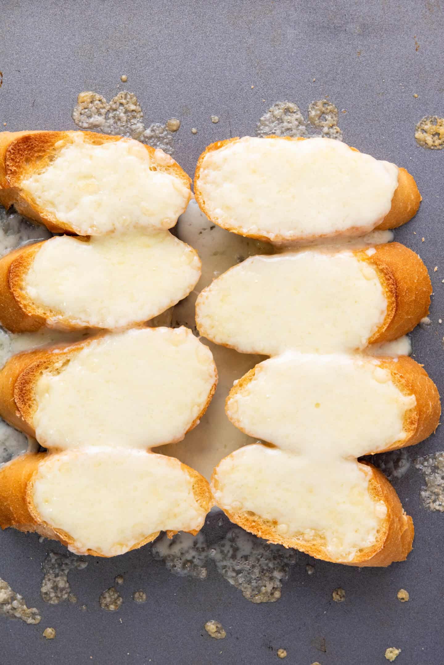 Eight slices of toasted baguette, inspired by classic French Onion Soup, are topped with melted cheese and arranged on a baking tray.