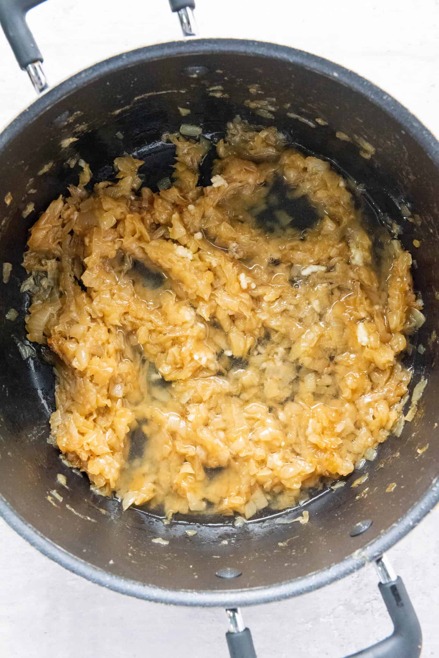 Chopped onions cooking and caramelizing in a black pot, with some liquid visible at the bottom—perfect as the flavorful base for French Onion Soup.