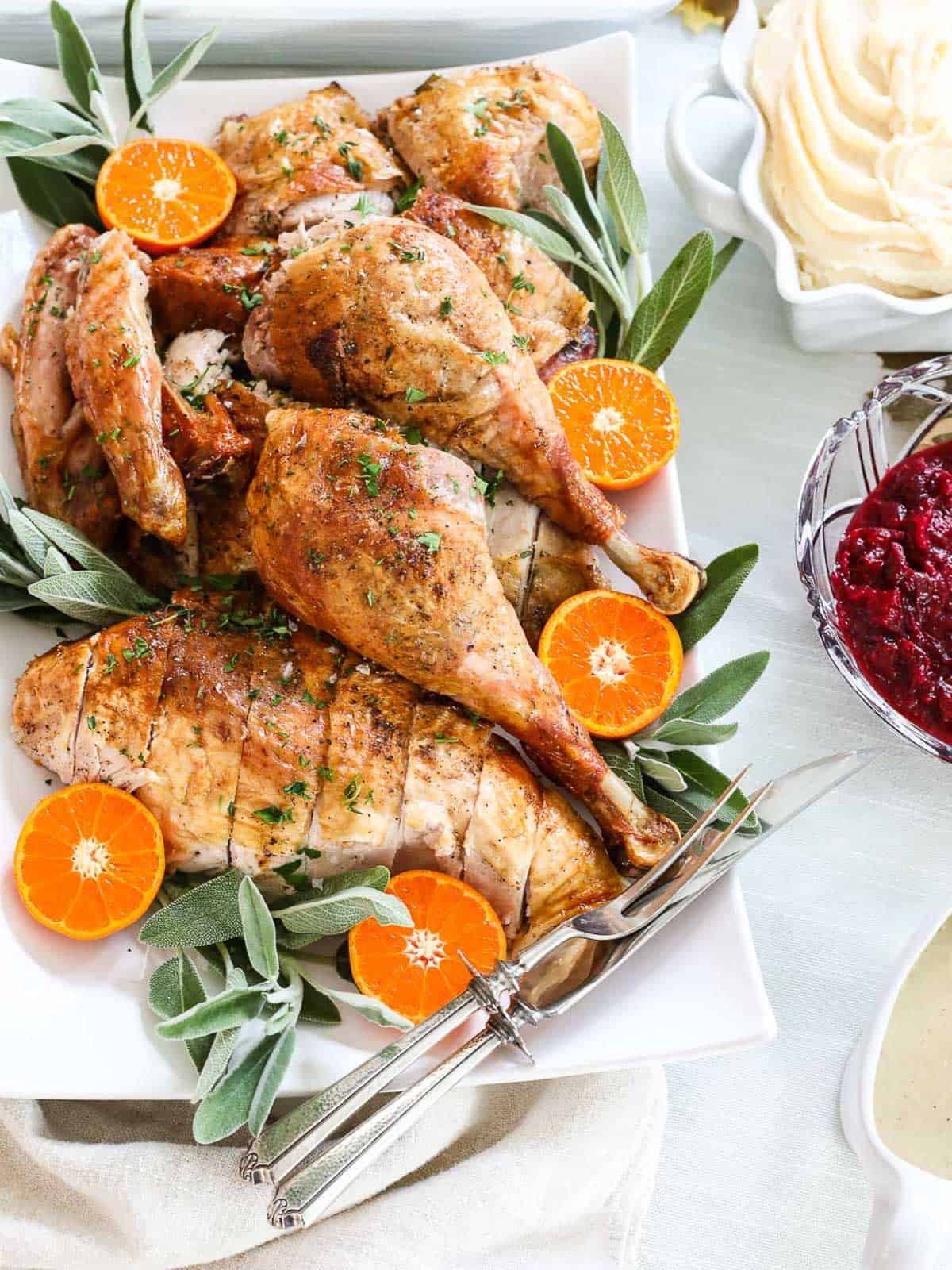 Roast turkey pieces garnished with herbs and sliced mandarins on a platter, served alongside mashed potatoes, cranberry sauce, and gravy—a festive highlight from our Christmas Dinner Menu.