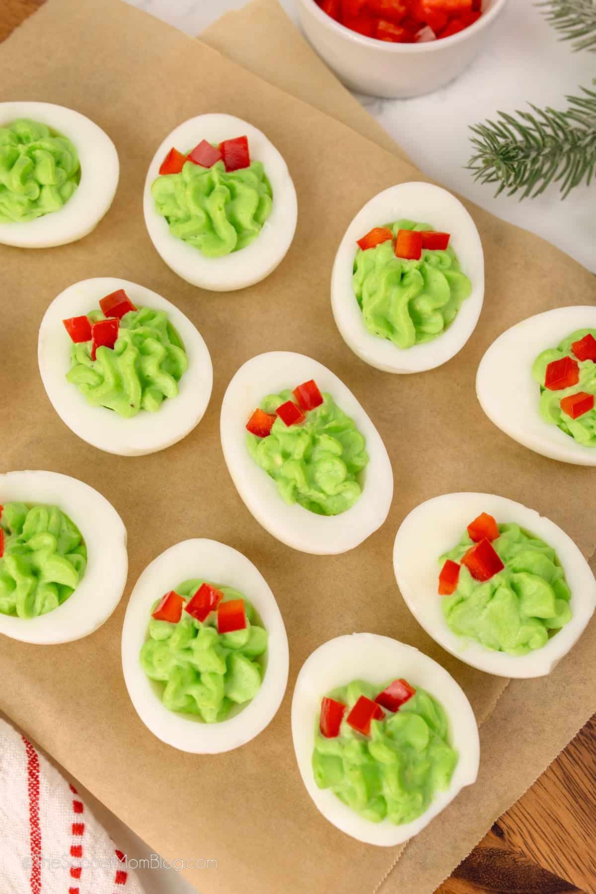 Deviled eggs with green filling, garnished with red bell pepper, arranged on parchment paper—a festive addition to your Christmas Dinner Menu.