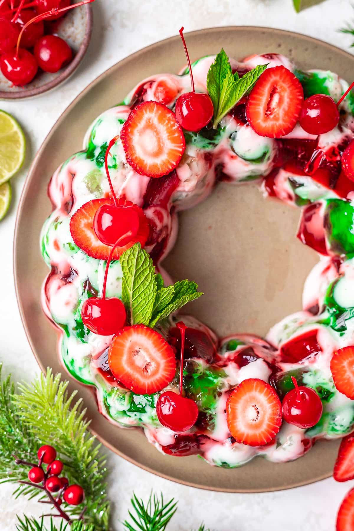 A festive gelatin mold ring with red and green jello, topped with fresh strawberries, cherries, and mint leaves—this cheerful dessert is perfect for any Christmas Dinner Menu, served beautifully on a round plate.