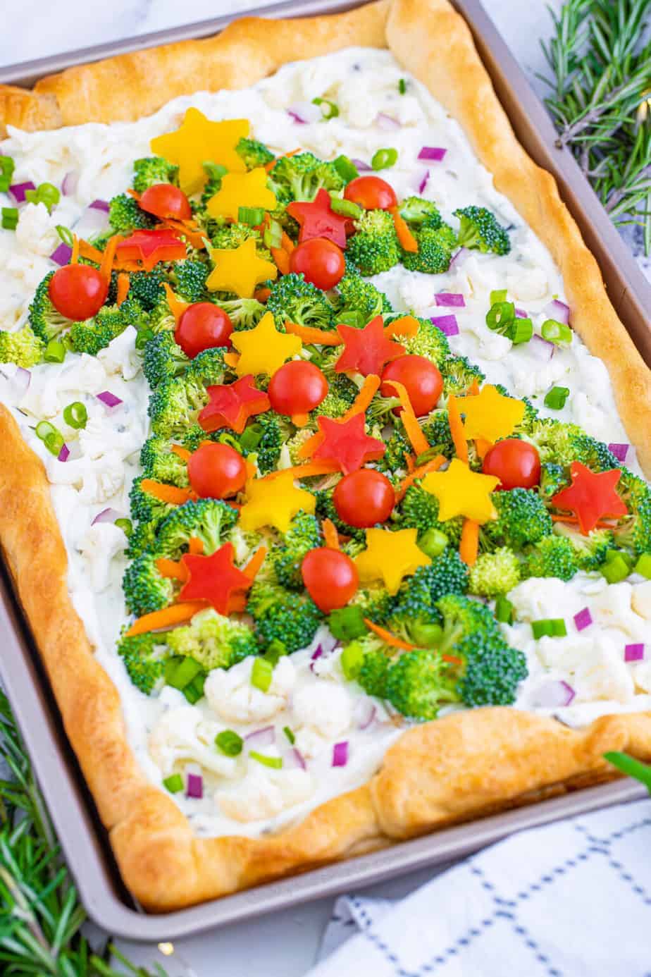 Rectangular veggie pizza shaped like a Christmas tree, topped with broccoli, cherry tomatoes, and star-shaped yellow peppers on a cream cheese base—an eye-catching addition to your Christmas Dinner Menu.