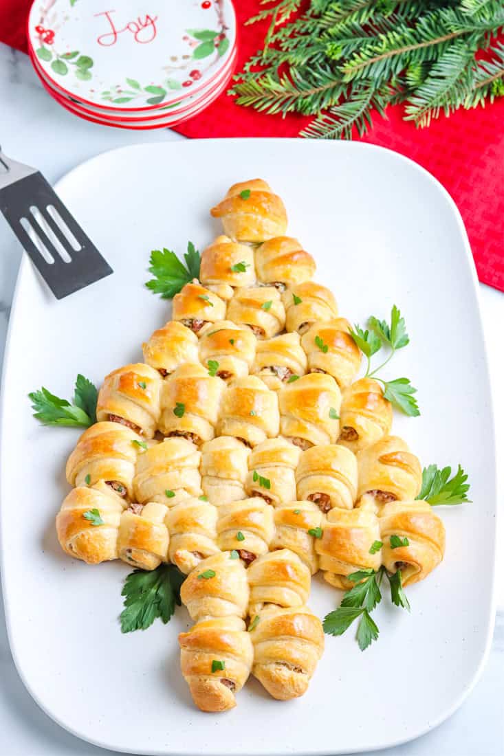 A festive pastry appetizer shaped like a Christmas tree, made of crescent rolls and garnished with parsley, adds charm to any Christmas Dinner Menu when arranged on a white platter.