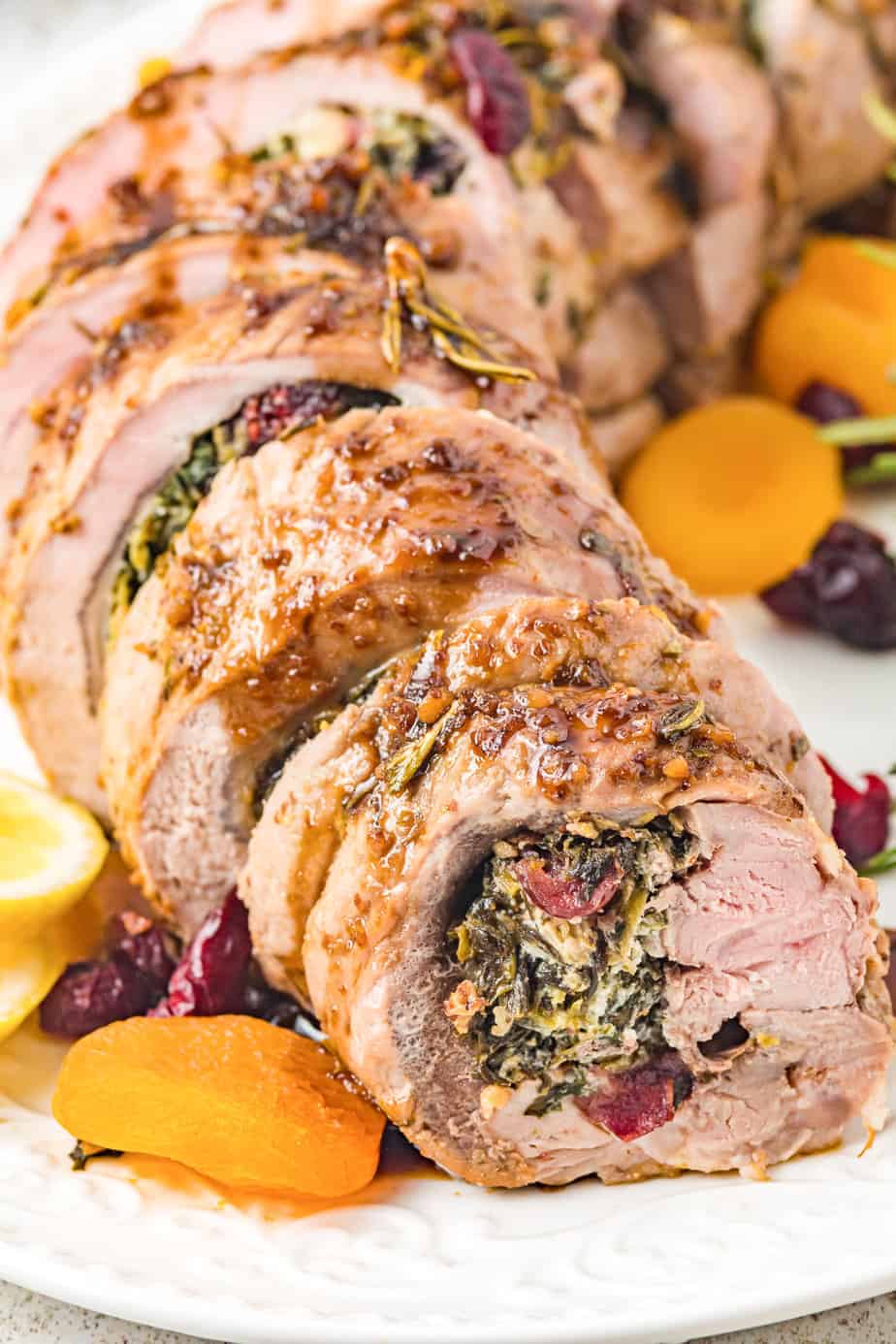 Sliced stuffed pork tenderloin with herb and fruit filling, garnished with dried apricots and cranberries on a white plate—a festive highlight for any Christmas Dinner Menu.