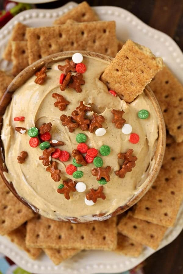 A bowl of creamy dip topped with gingerbread-shaped and round red, white, and green sprinkles, surrounded by square graham crackers—an irresistible addition to your Christmas Dinner Menu.