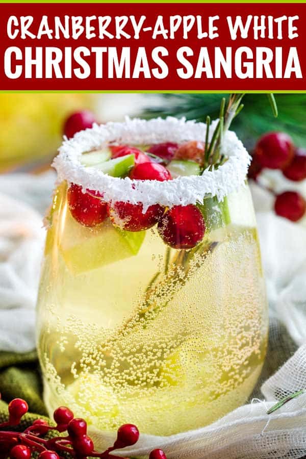 A glass of white sangria with cranberries and apple chunks, rimmed with coconut, sits on a table with festive decorations—perfect for your Christmas Dinner Menu.