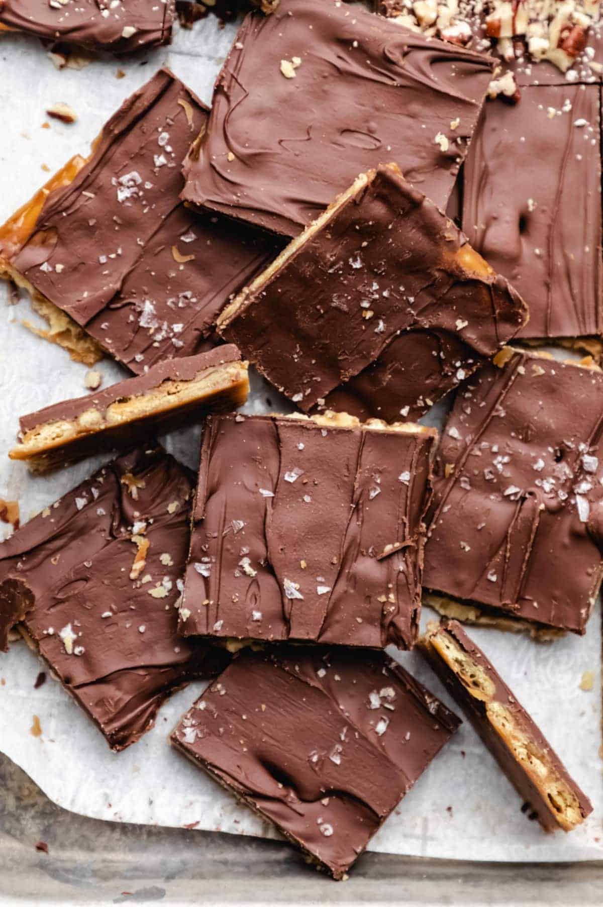 Squares of chocolate toffee bark with a visible layer of caramel and nuts, topped with flaky sea salt, arranged on parchment paper—an irresistible treat perfect for your Christmas Dinner Menu.