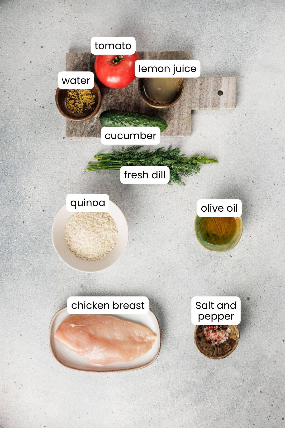 Top-down view of labeled Mediterranean ingredients on a counter: tomato, cucumber, fresh dill, quinoa, chicken breast for a Chicken Bowl, olive oil, lemon juice, water, salt, and pepper.
