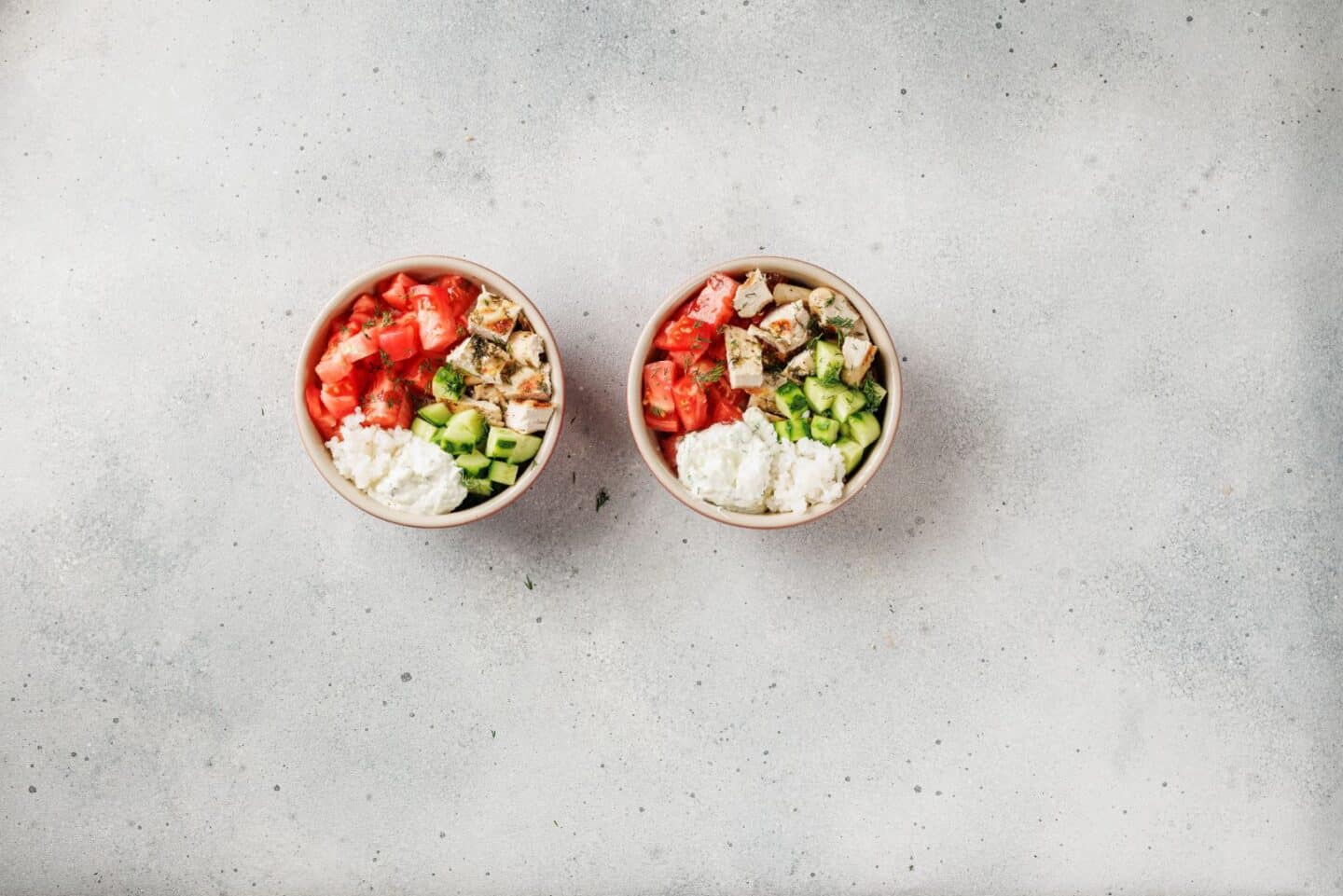 Two Mediterranean chicken bowls featuring rice, Lemon-Dill Chicken, chopped tomatoes, and sliced cucumbers, beautifully arranged on a light gray surface.