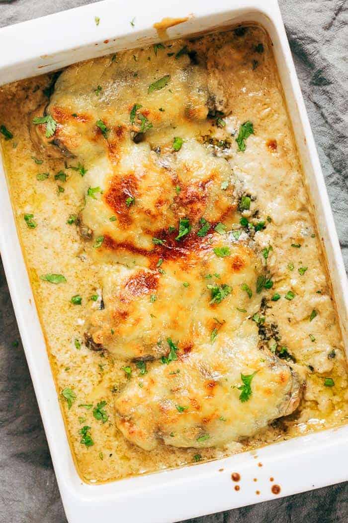 Baked chicken breasts covered in melted cheese and creamy sauce, garnished with chopped herbs, make a perfect addition to your Sunday Dinner Ideas, all served in a white rectangular baking dish.